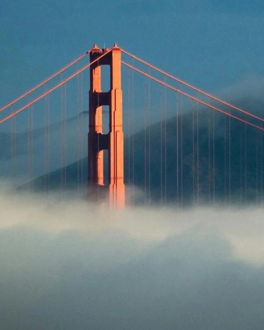 Golden Gate Bridge partially obscured by fog with clear sky background.