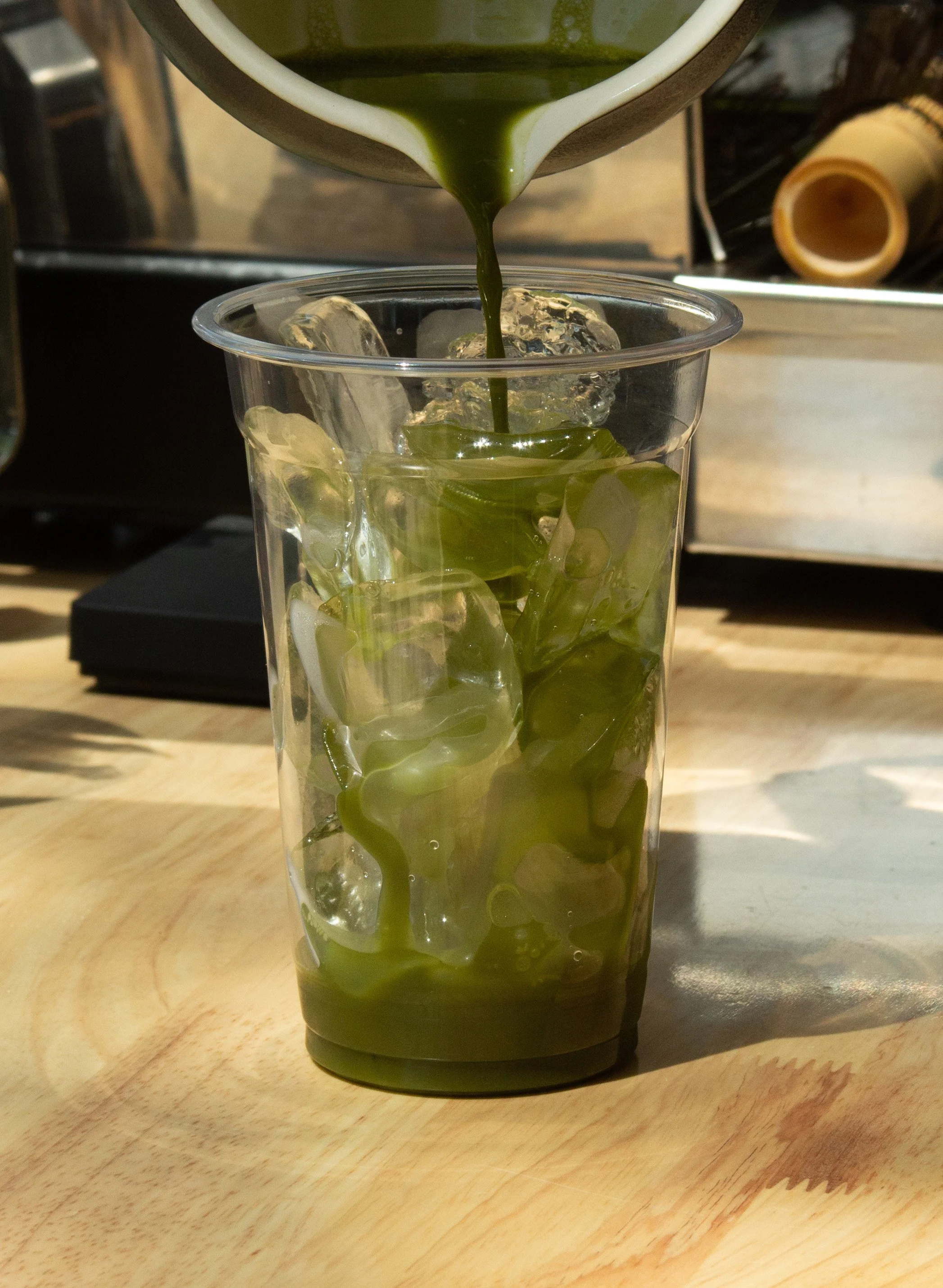 Tall glass filled with ice and matcha green tea, with green tea being poured from a bowl above.