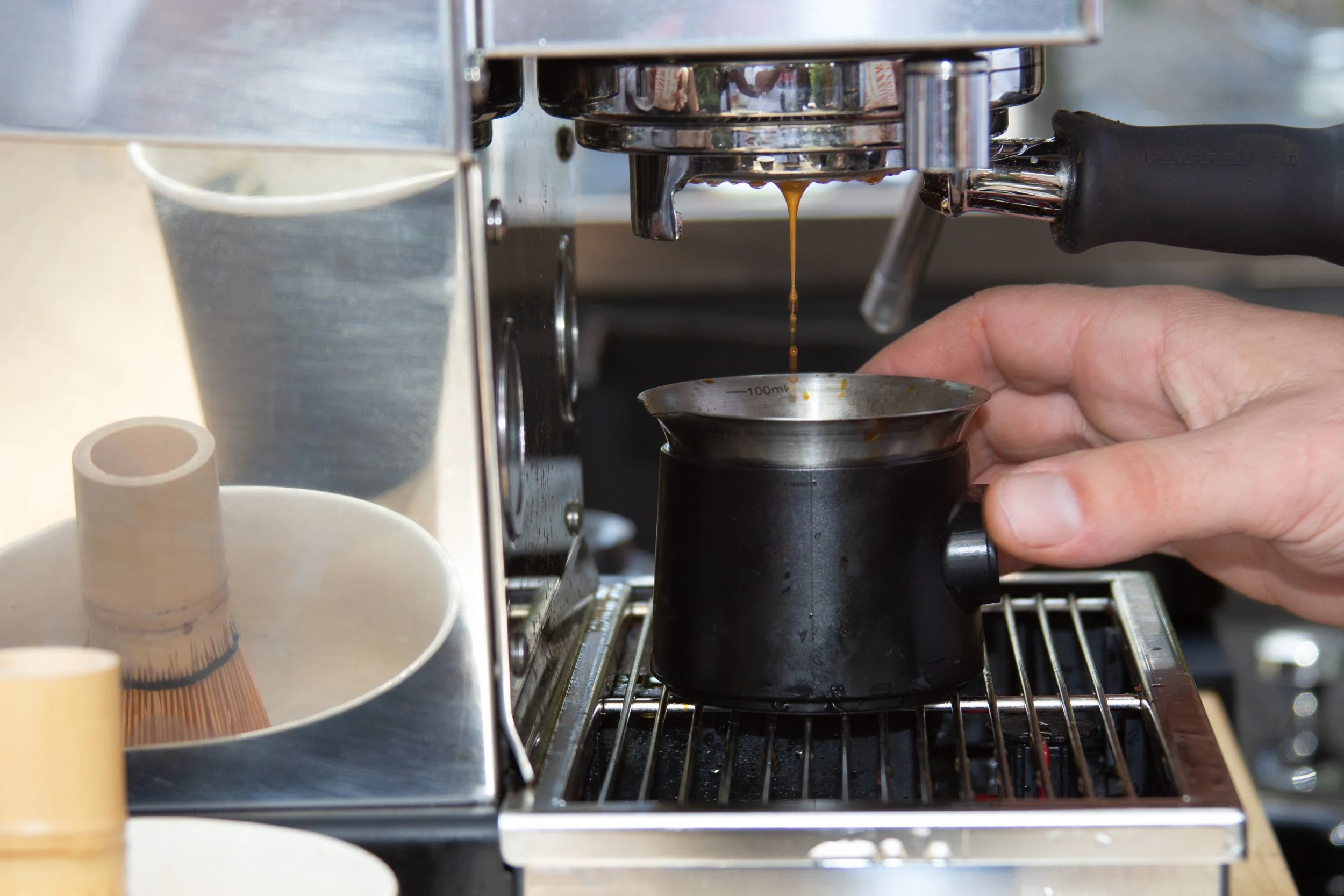 Close-up of a coffee espresso machine dispensing coffee into a small metal cup, with a person's hand supporting the cup.