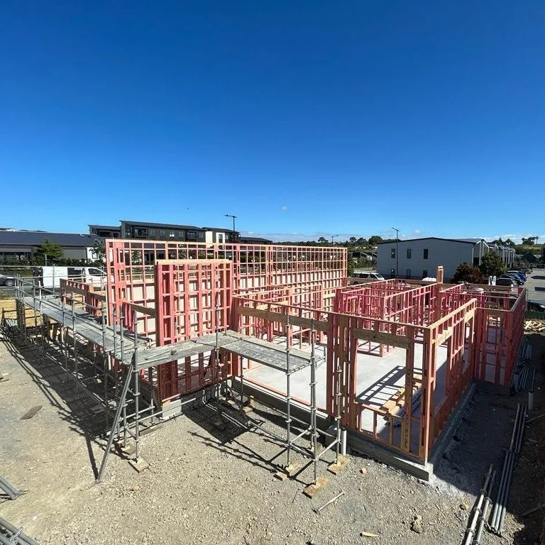 Construction site with pink framing for a building, partially built with scaffolding around it, under a clear blue sky.