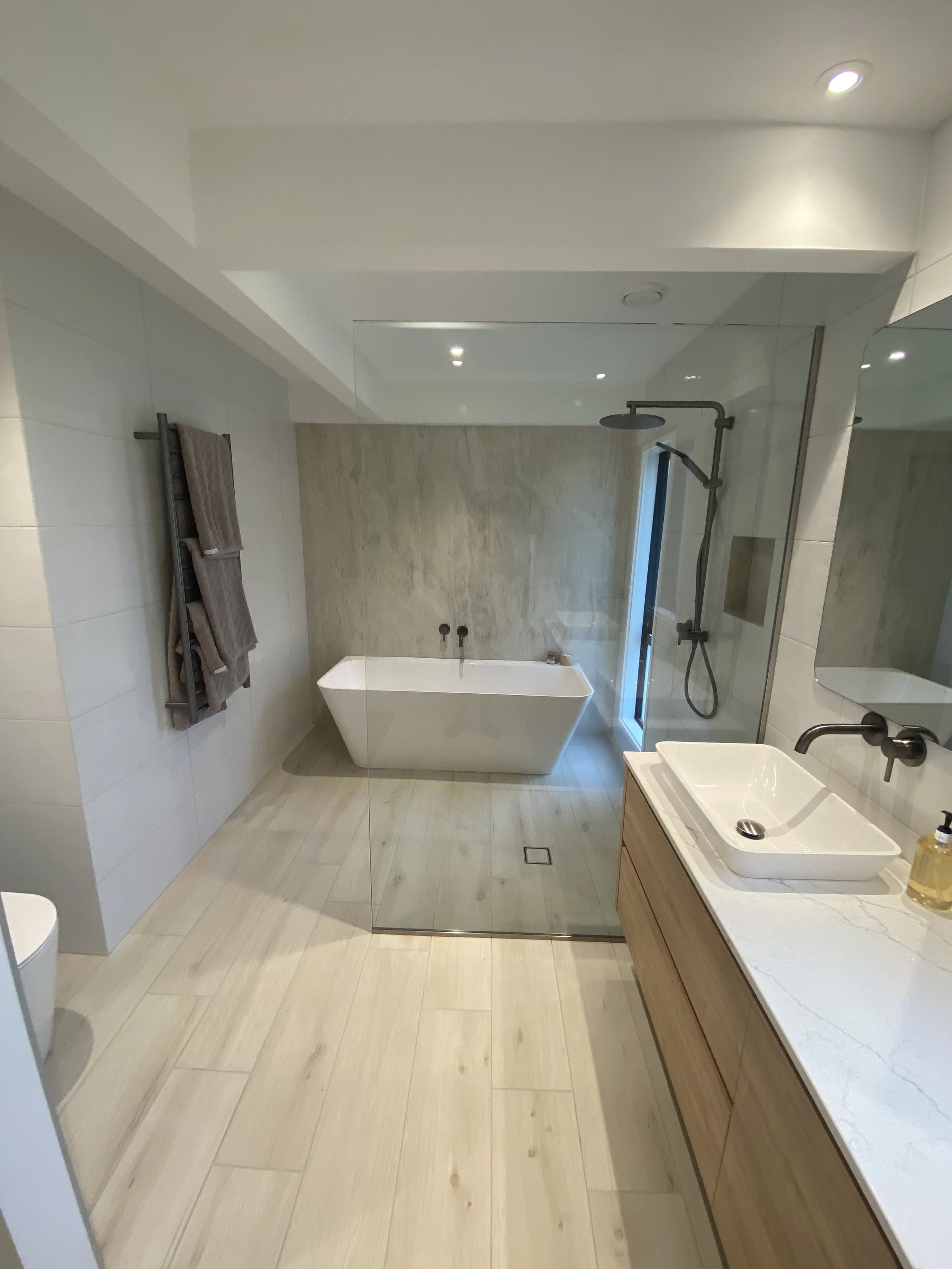 Modern bathroom with a walk-in shower, freestanding bathtub, wooden vanity with vessel sink, and beige marble accents.