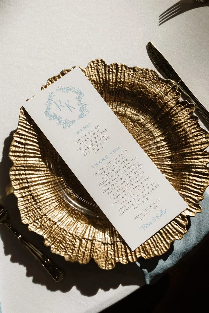 A wedding menu and a thank you note placed on a decorative gold-colored plate, with a fork and knife nearby.