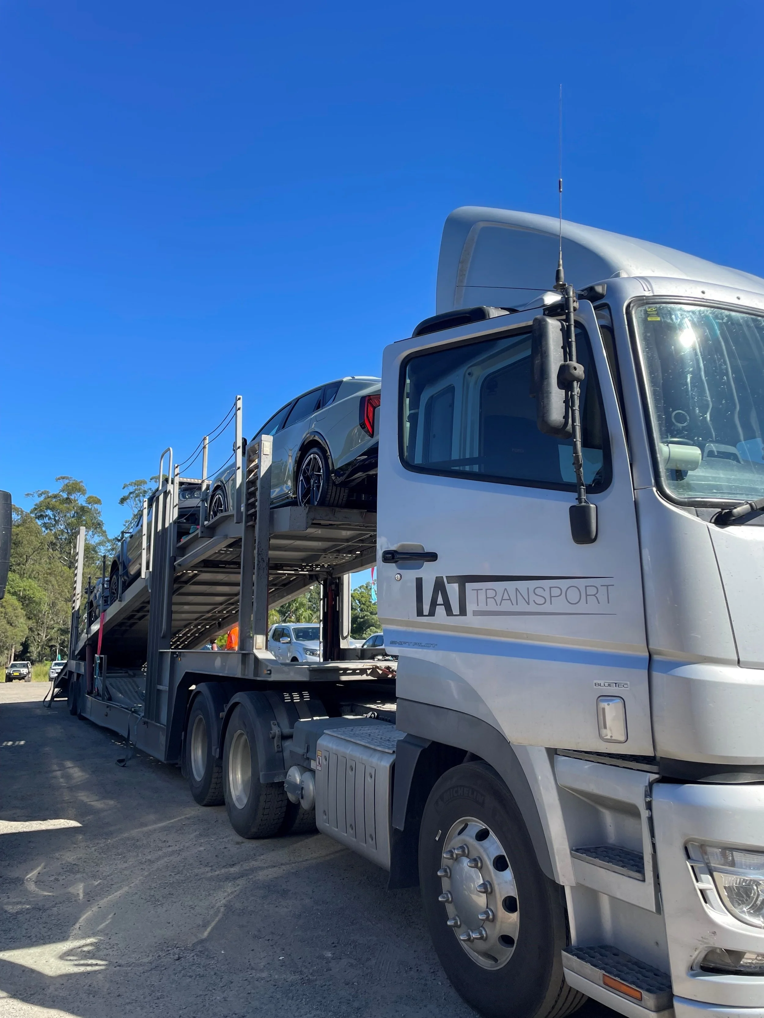 A semi-truck transporting two cars on a car carrier trailer against a clear blue sky.
