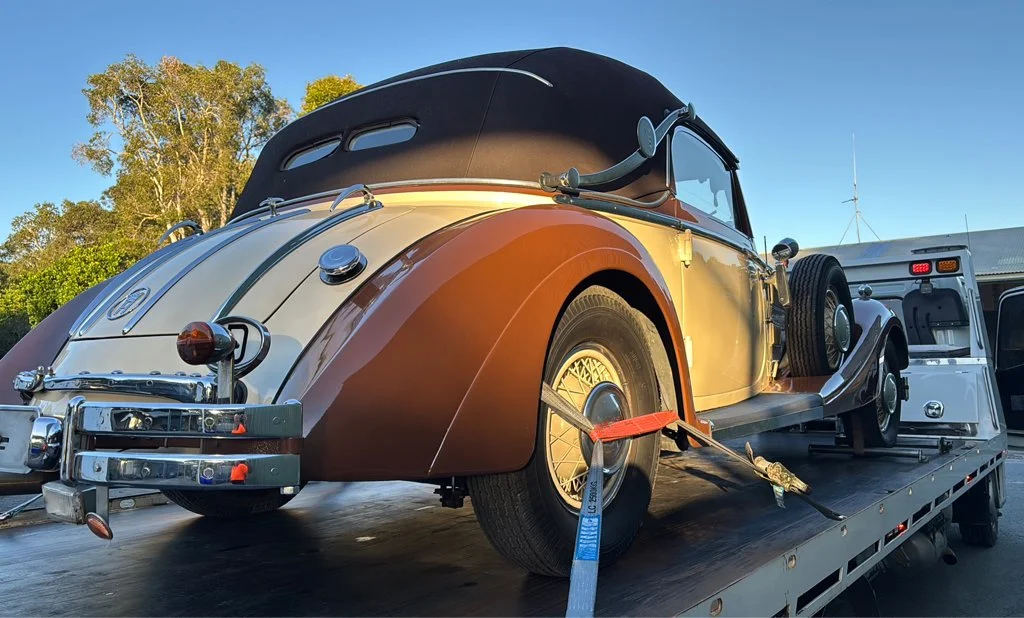 Vintage two-tone convertible car secured on a flatbed truck with trees in the background.