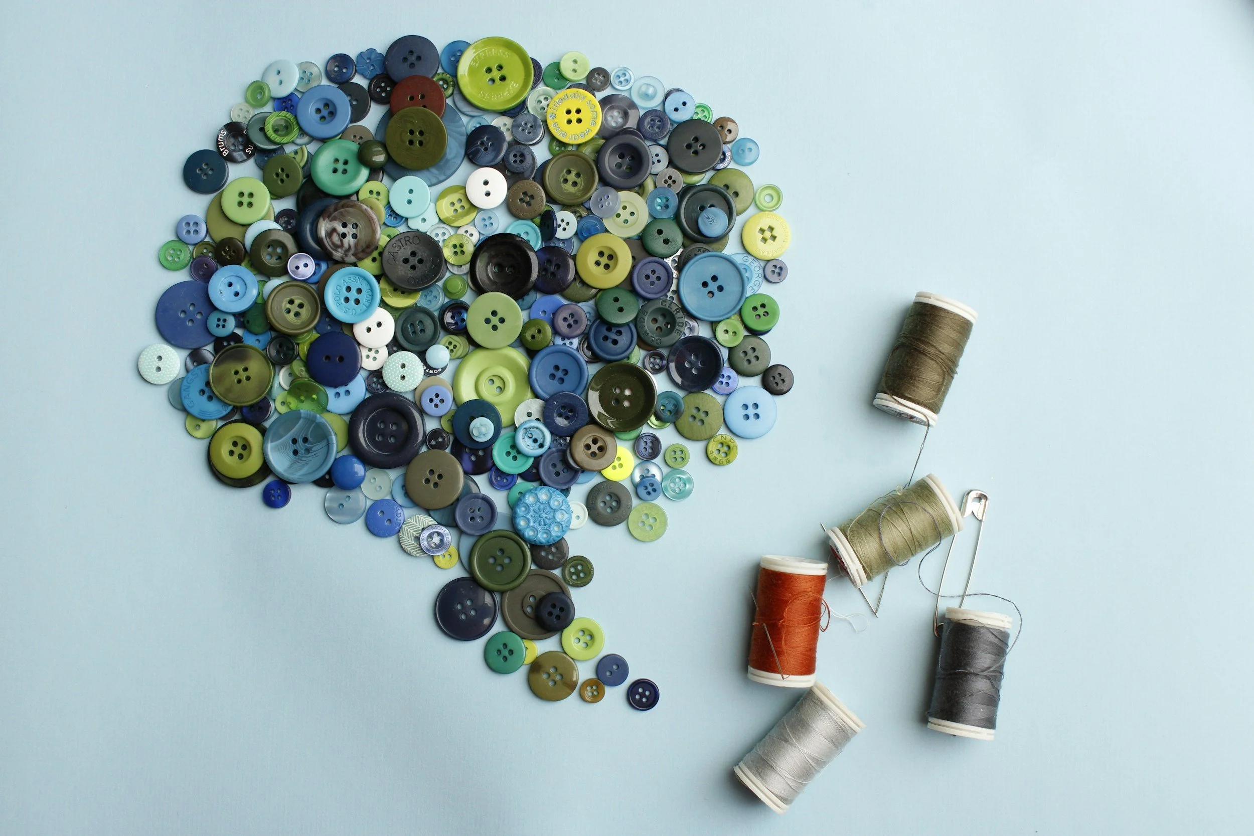 An assortment of colorful buttons of various sizes scattered on a light blue background, alongside spools of sewing thread in different colors.