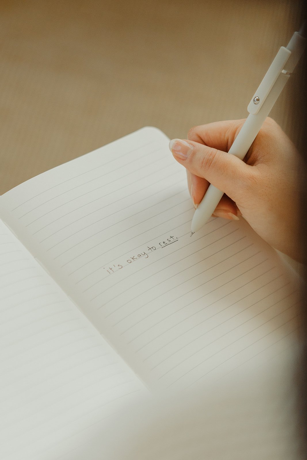 A person writing in a notebook with a pen that reads, 'It's okay to rest.'