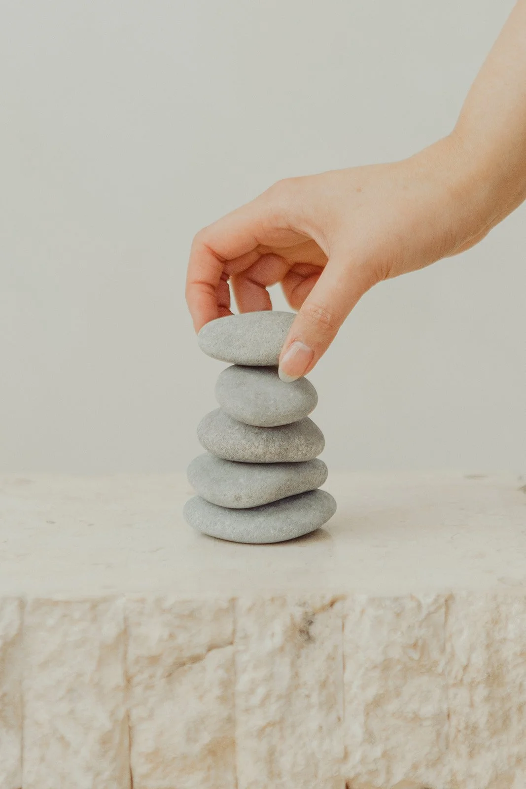 A hand stacking smooth gray stones on a light-colored surface indoors.