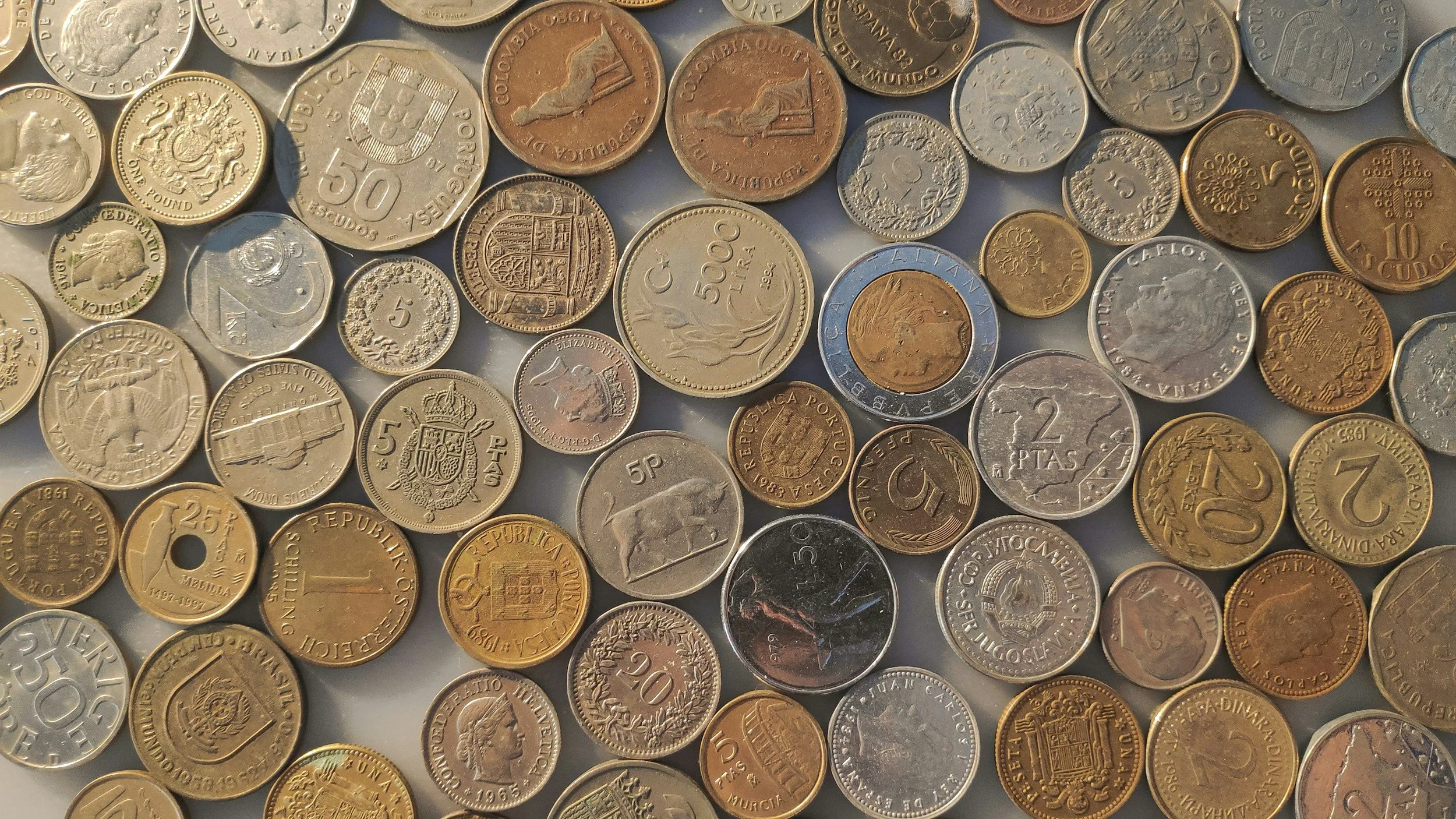 A collection of various international coins of different denominations, sizes, and colors scattered on a surface.