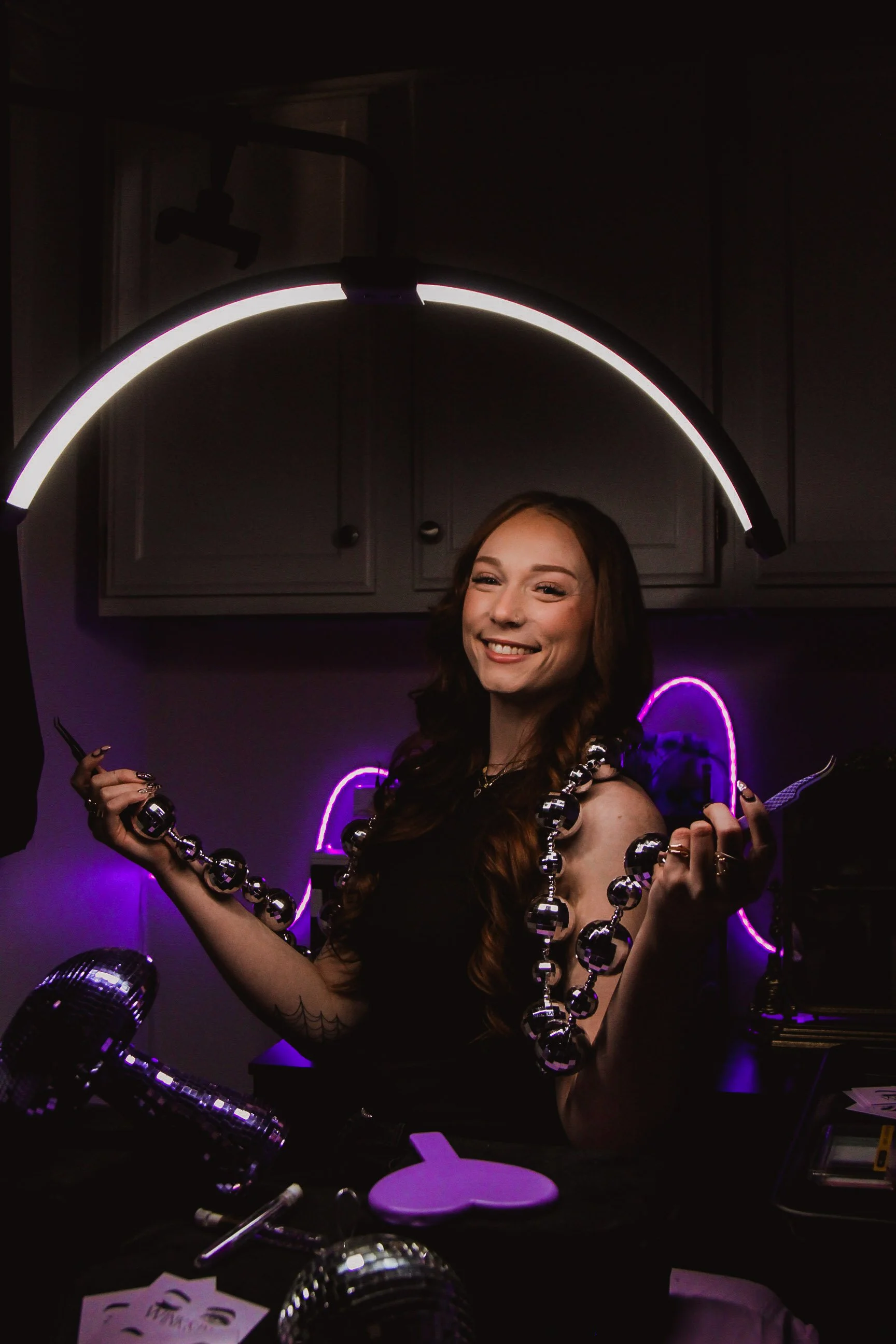 owner of wink&ink studio in tulsa oklahoma holding tweezers in an aestheticly lit dark room with purple accents