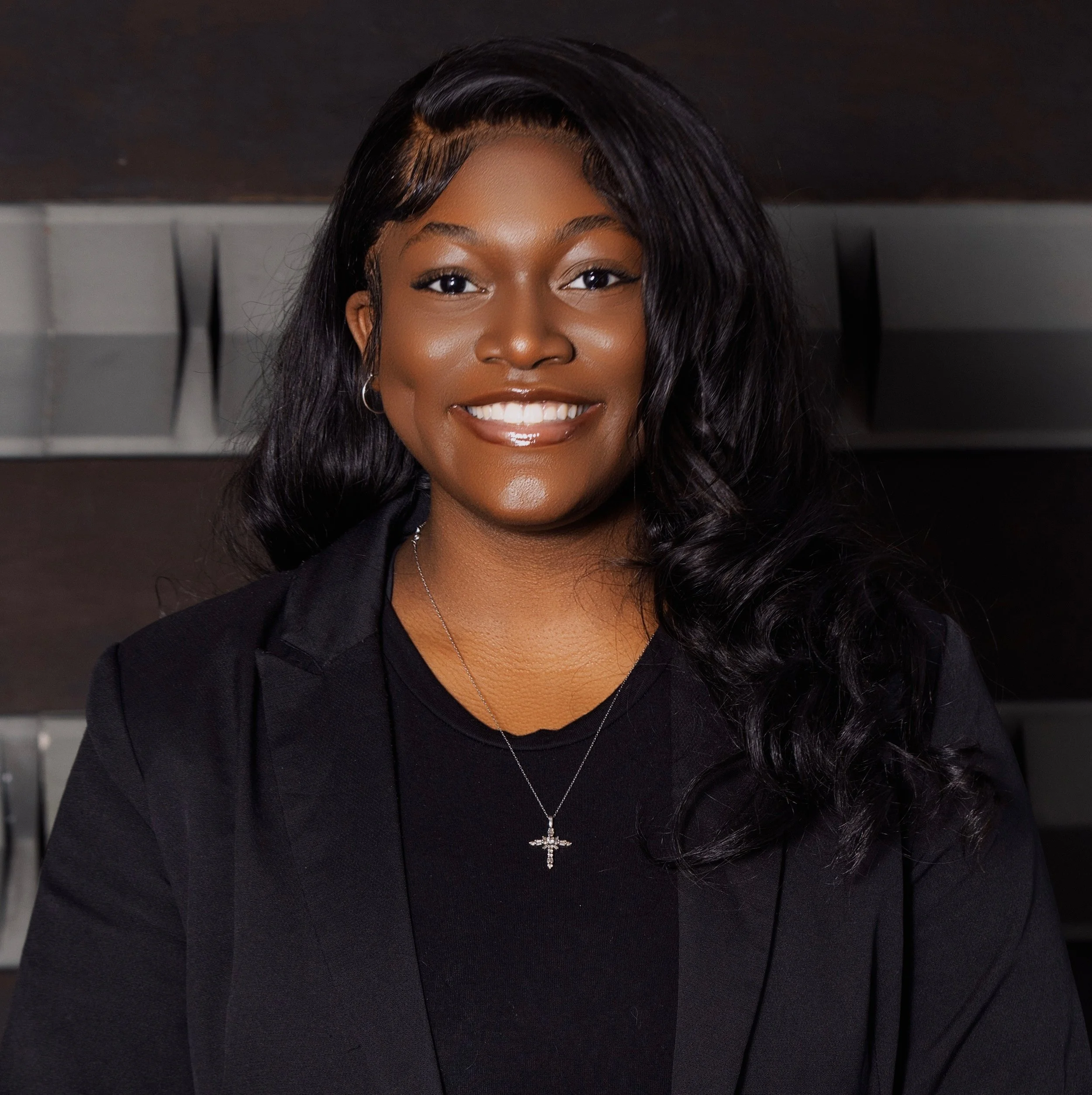 A smiling young Black woman with long black hair dressed in formal black attire.