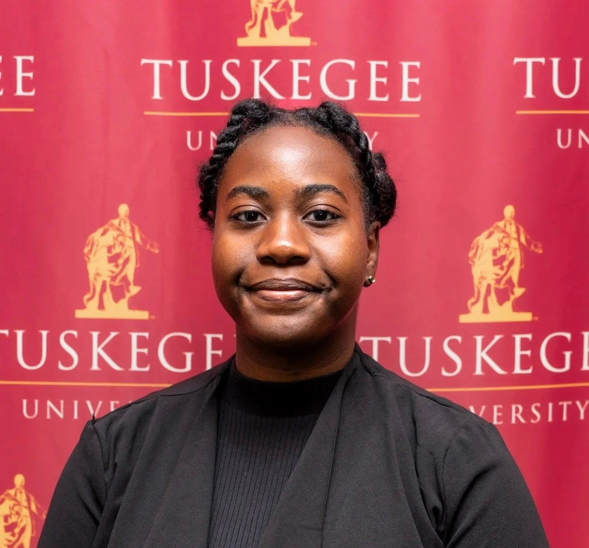 A young women with a black shirt in front of a Tuskegee background.