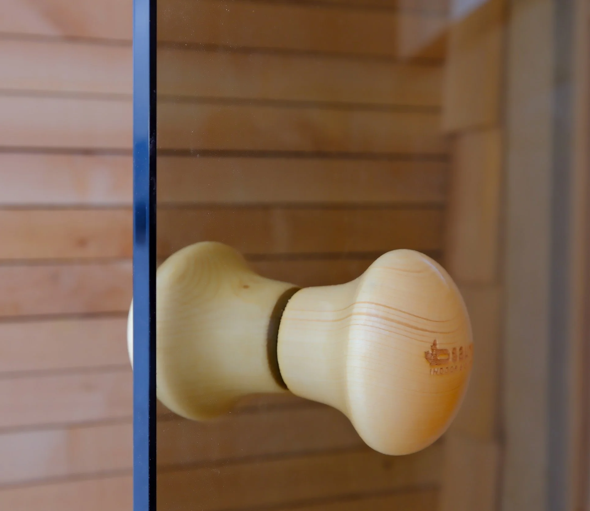 A close-up view of a yellowish wooden door knob attached to a glass door, with a wooden wall background.