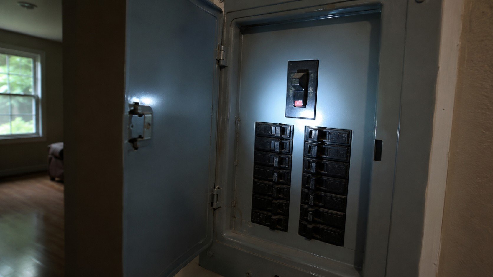 Home electrical panel with a tripped main breaker lit by a flashlight