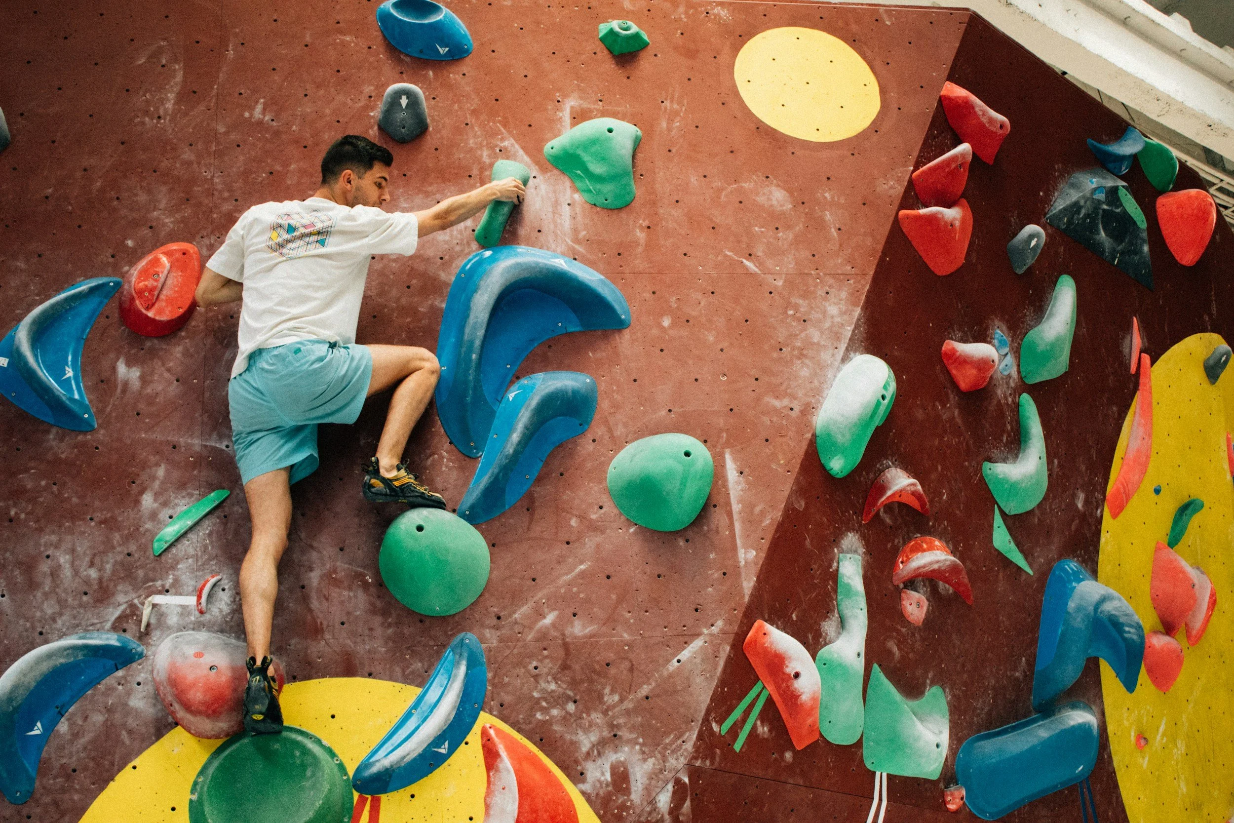 A man climbing an indoor bouldering wall with colorful holds.