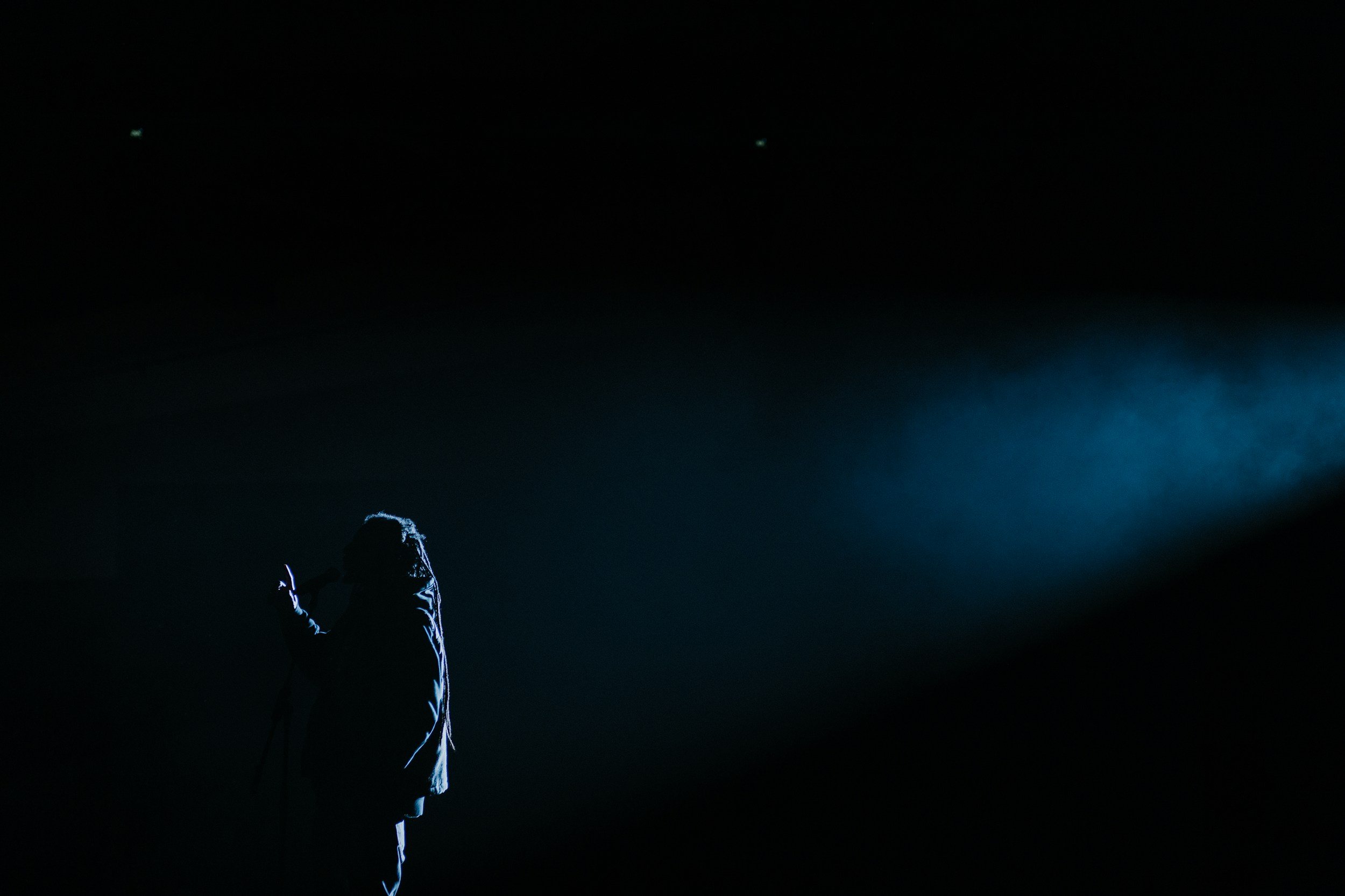 Silhouette of a singer with a microphone on a dark stage, illuminated by a spotlight