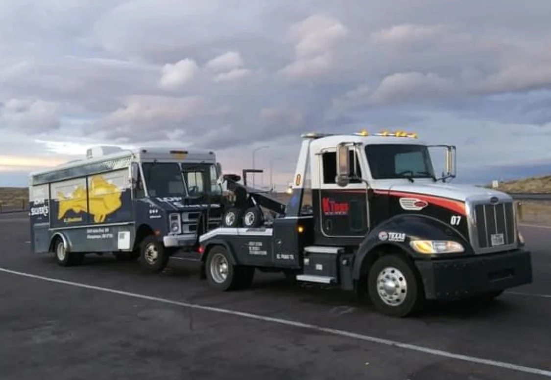 Semi-truck towing a recreational vehicle with a yellow dog silhouette on its side, on a highway with cloudy sky.