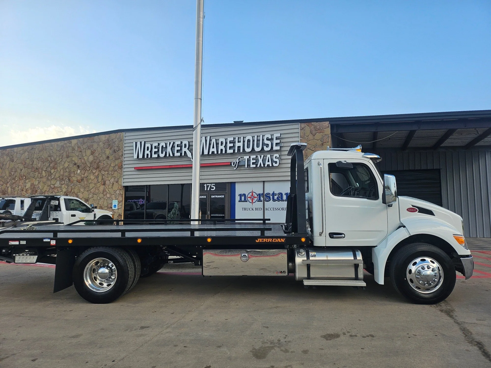 White flatbed truck parked in front of a building with a sign reading "Wrecker Warehouse of Texas".