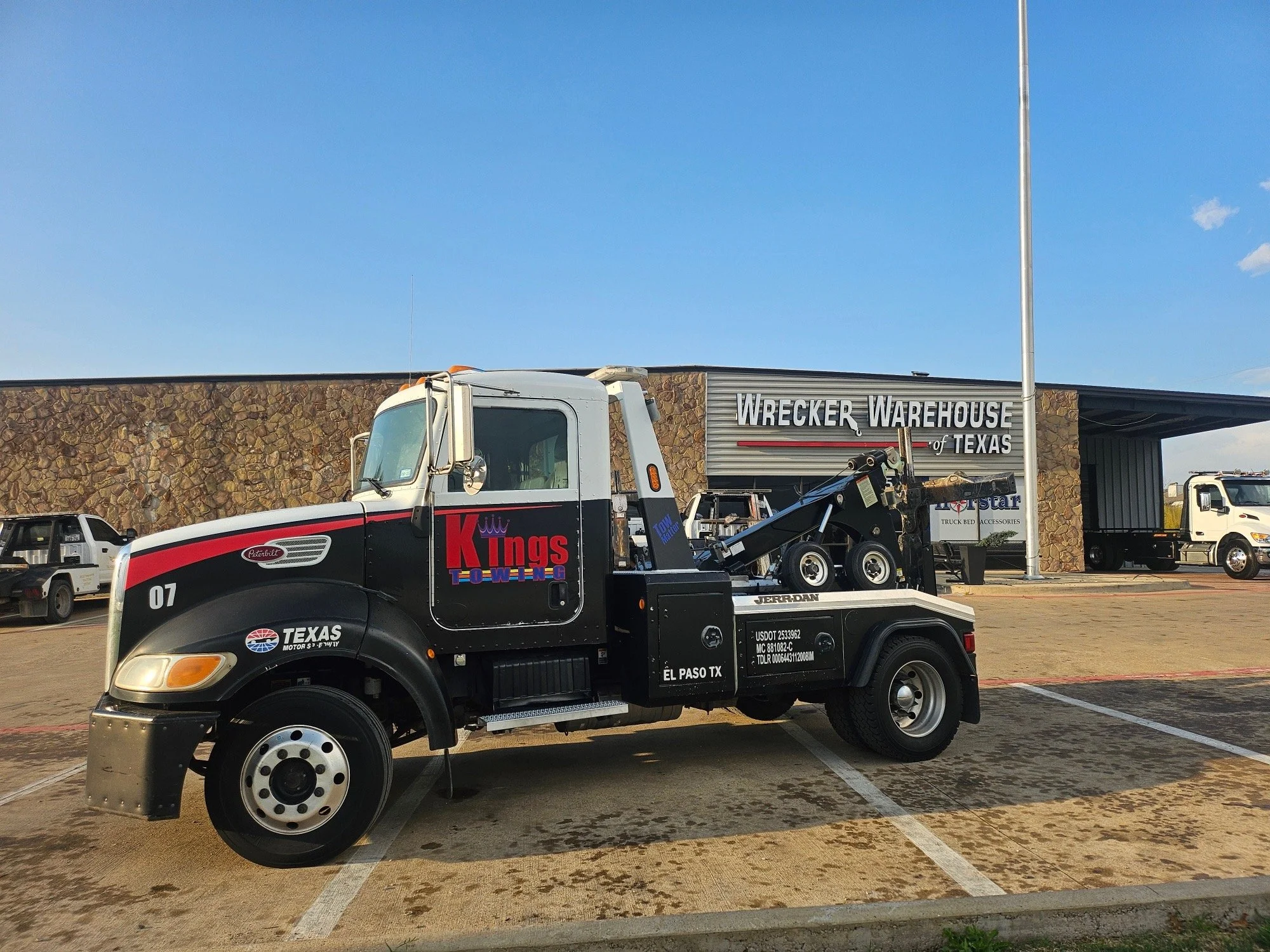 A tow truck parked in front of Wrecker Warehouse of Texas, with other vehicles in the background, on a sunny day.