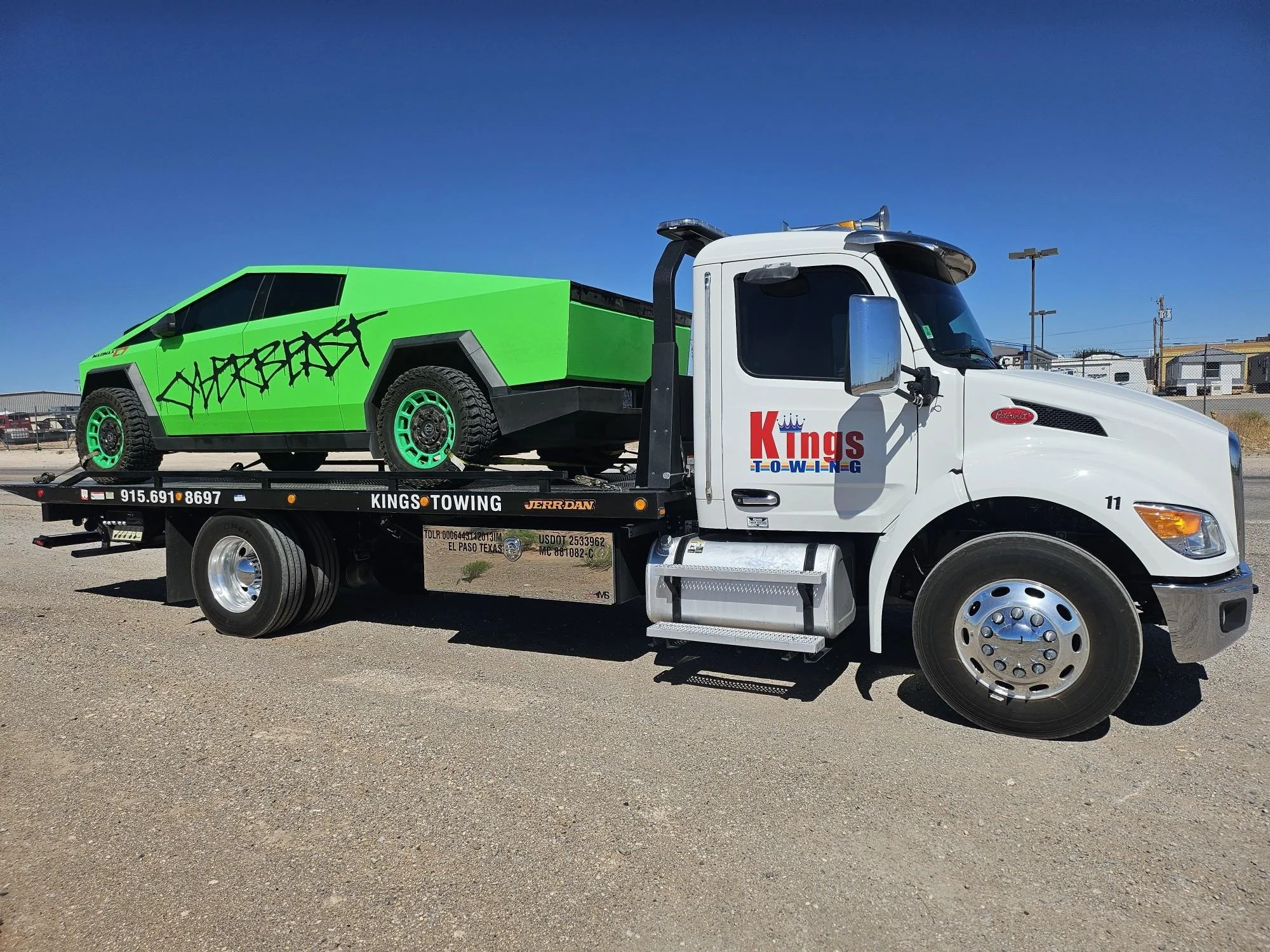 A white tow truck with "Kings Towing" logo on the door, carrying a bright green vehicle with graffiti-style writing on the side, and a blue sky in the background.