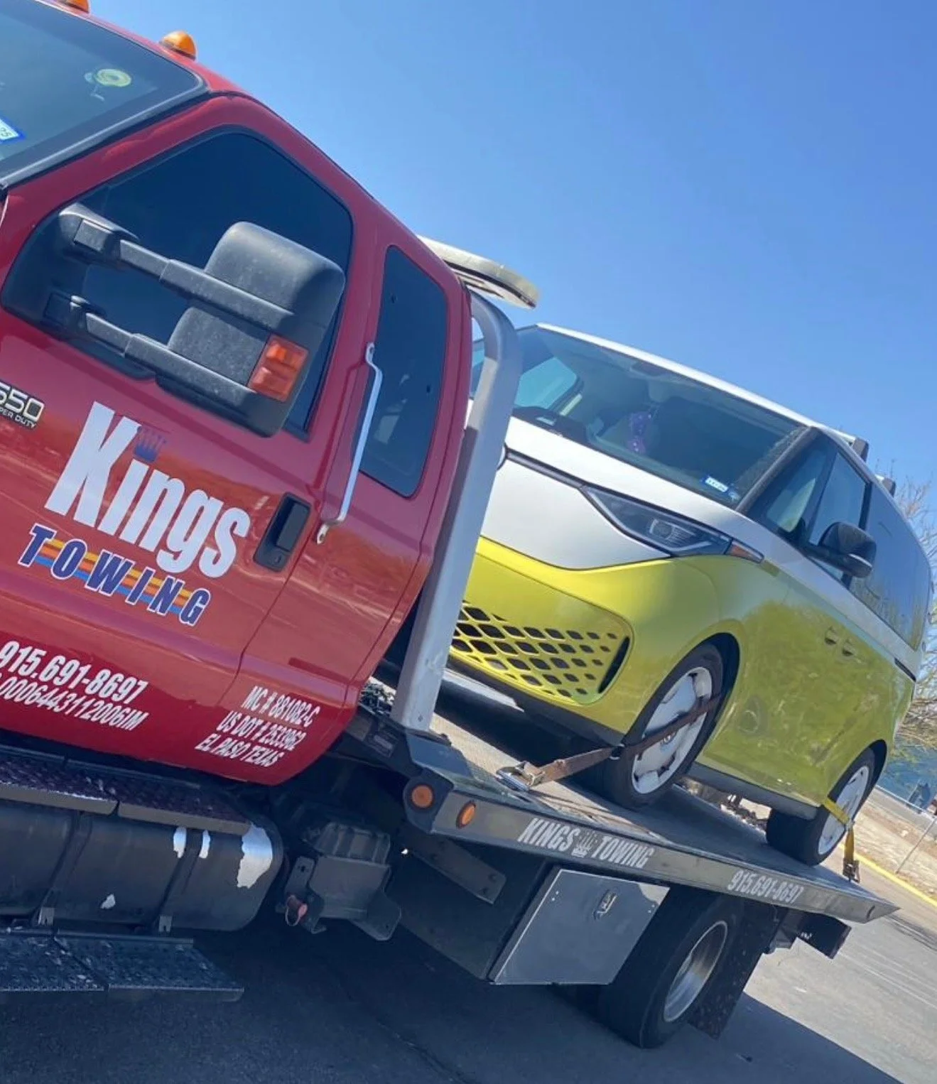 A tow truck carrying a green and white electric car with a yellow front. The tow truck has 'Kings Towing' written on the side.