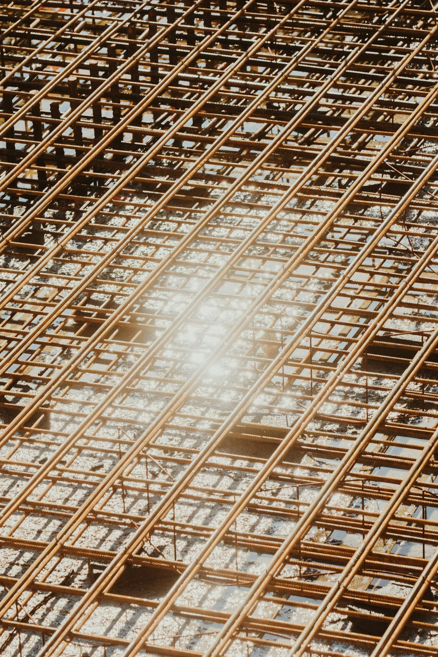 Close-up of a construction site showing rusted steel rebar grid with sunlight reflecting off of it.