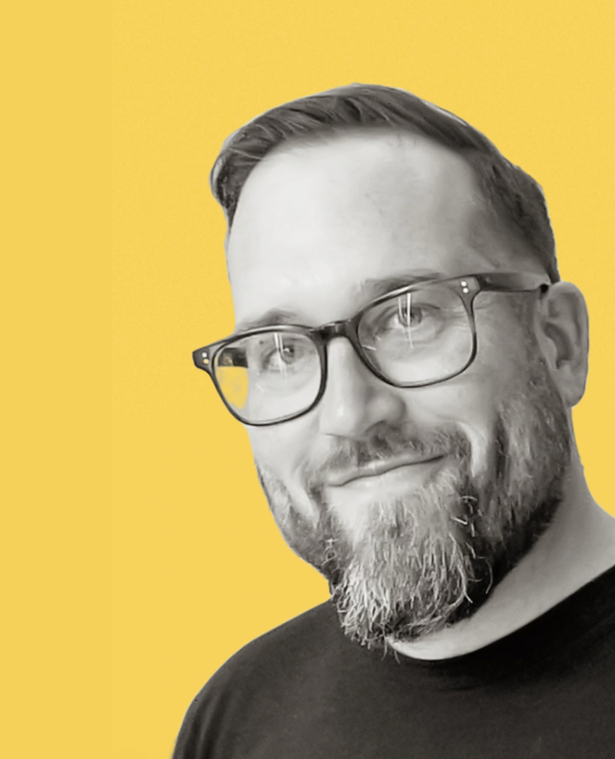 A man with glasses and a beard smiling, set against a yellow background.