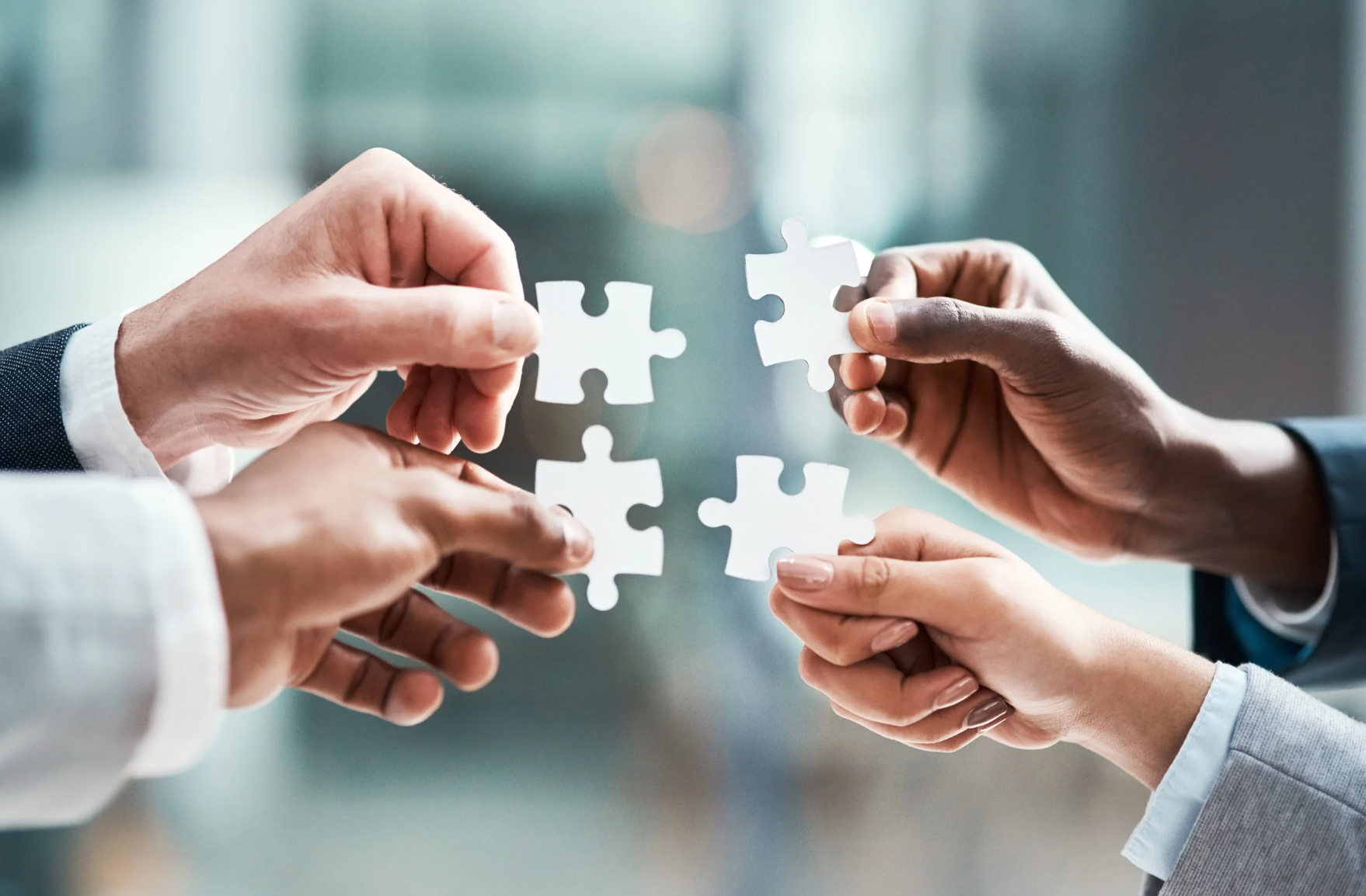 Four hands holding puzzle pieces coming together against a blurred background