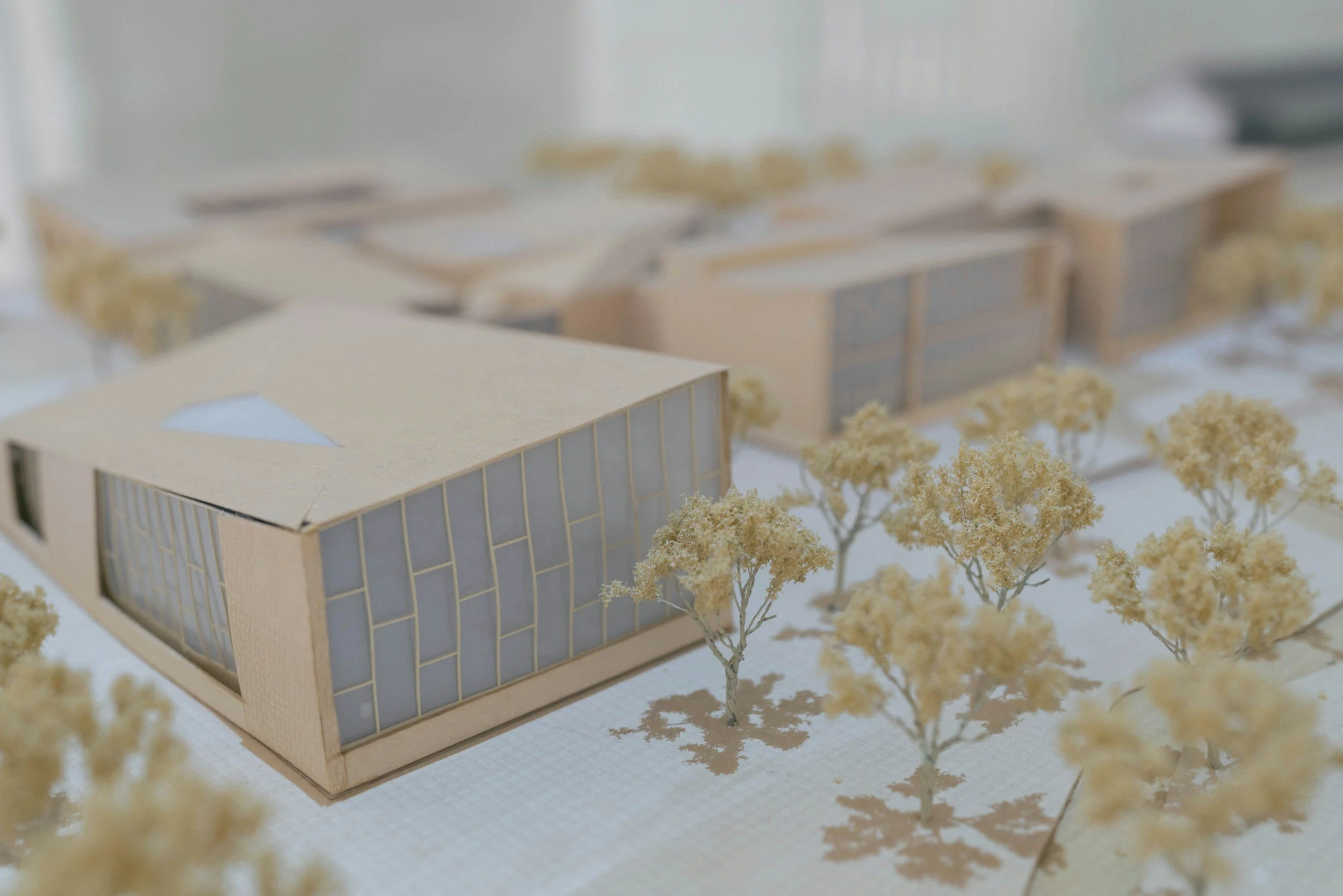 Architectural model of a modern building with large glass windows and surrounding trees.