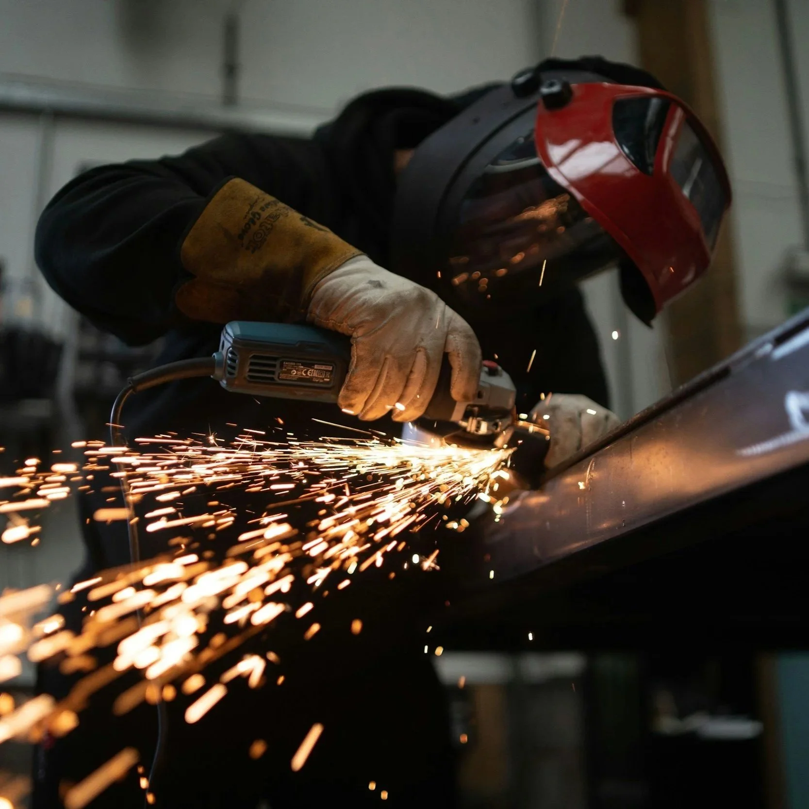 A person welding metal, wearing welding gloves and a protective helmet, sparks flying as they work on a metal piece.