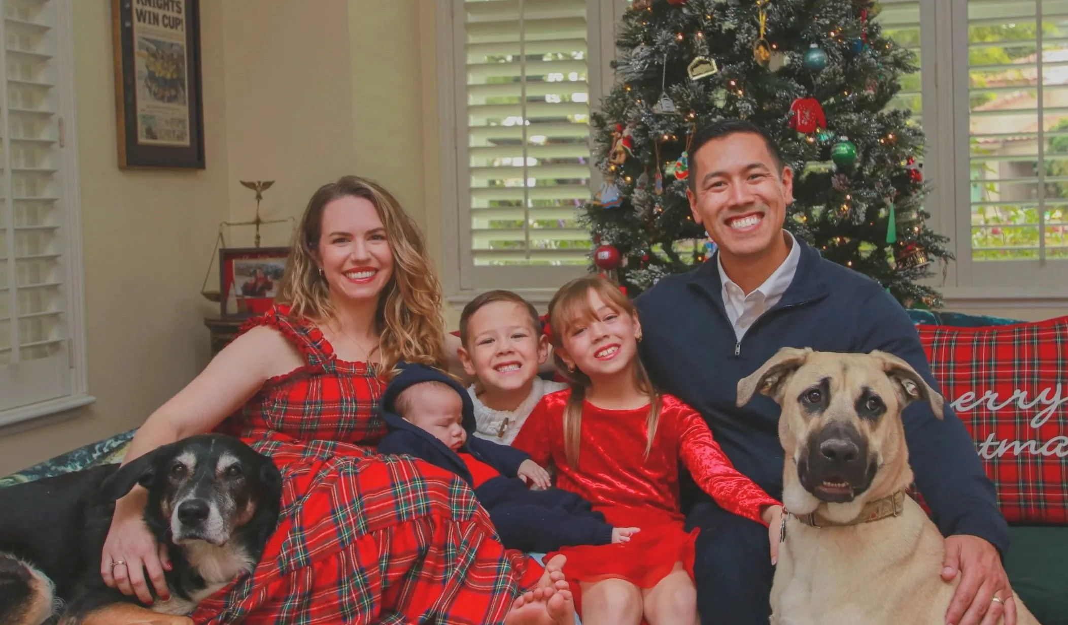 elect judicial candidate 8th judicial district court department 28 alex quagge Family celebrating Christmas with a decorated tree in the background, sitting on a couch with two dogs and three children, all smiling.