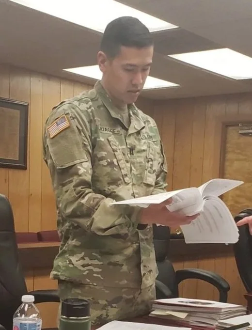 elect judicial candidate 8th judicial district court department 28 alex quagge is a  soldier in camouflage uniform reading a book or document in a army JAG courtrooom.