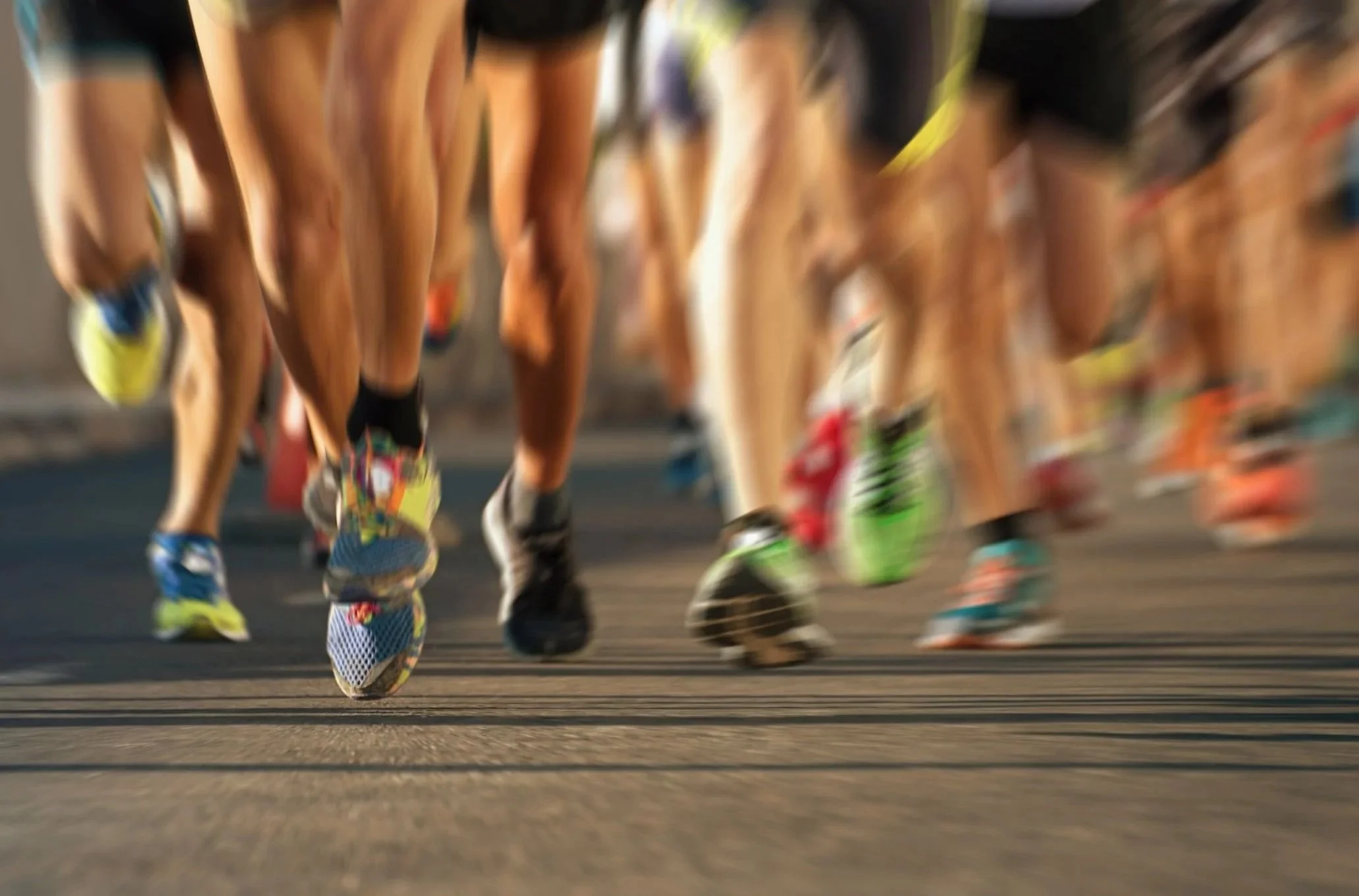 Close-up shot of runners' legs and feet during a marathon, with focus on their colorful running shoes, on a paved road.
