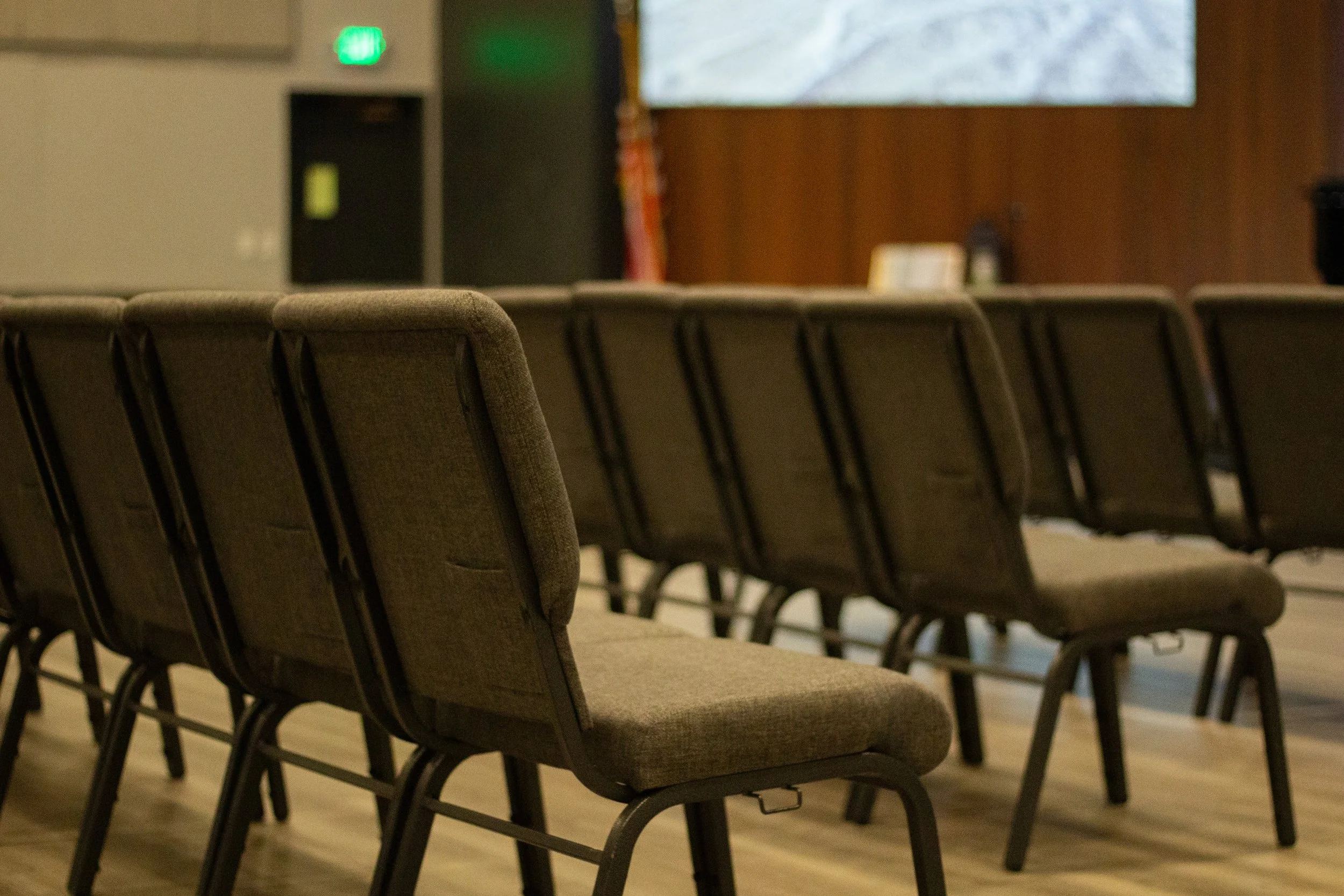 Empty conference room with brown upholstered chairs arranged in rows facing a large screen on a wooden wall.