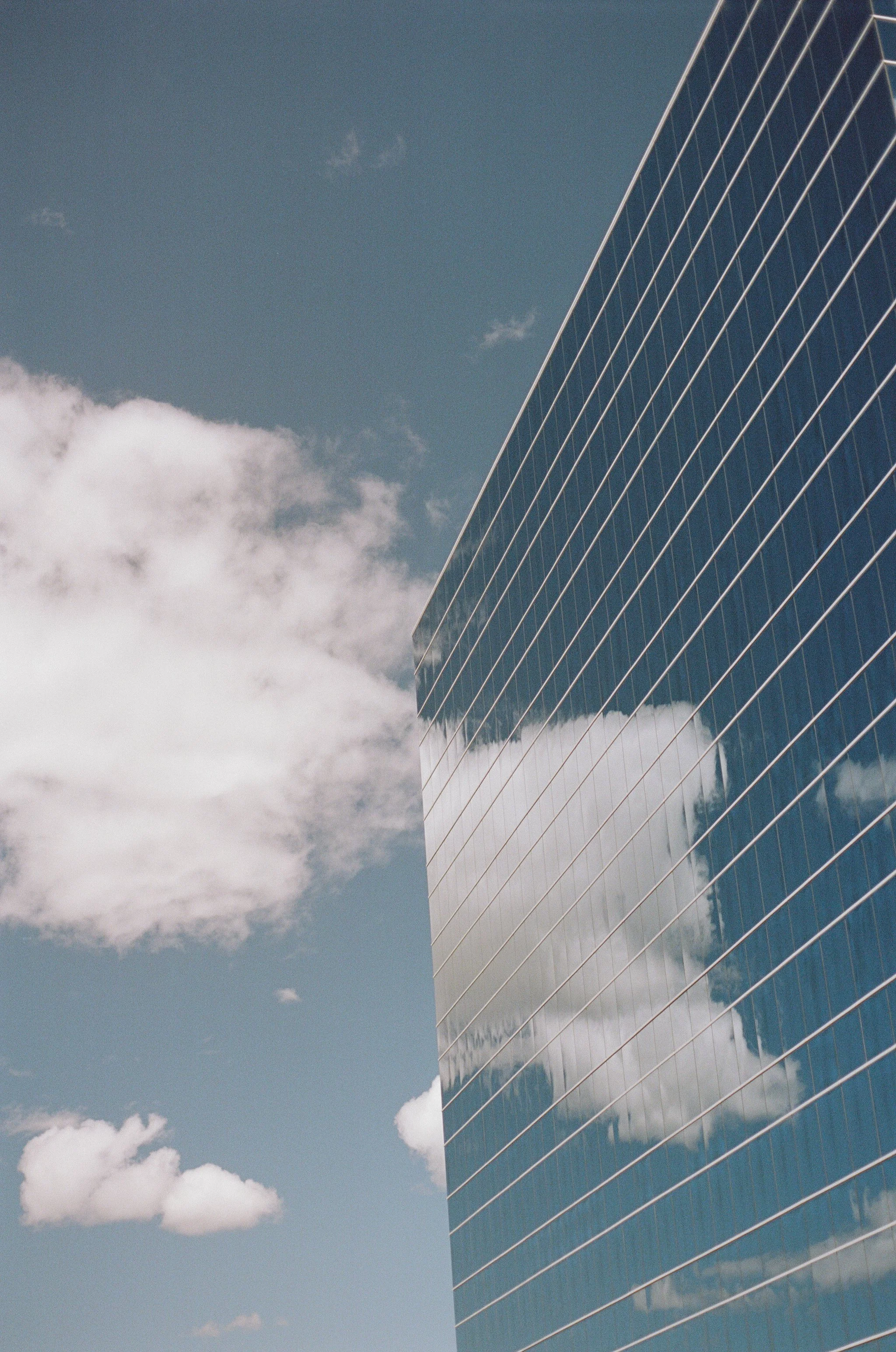 A modern glass building with reflective windows showing clouds in the sky.