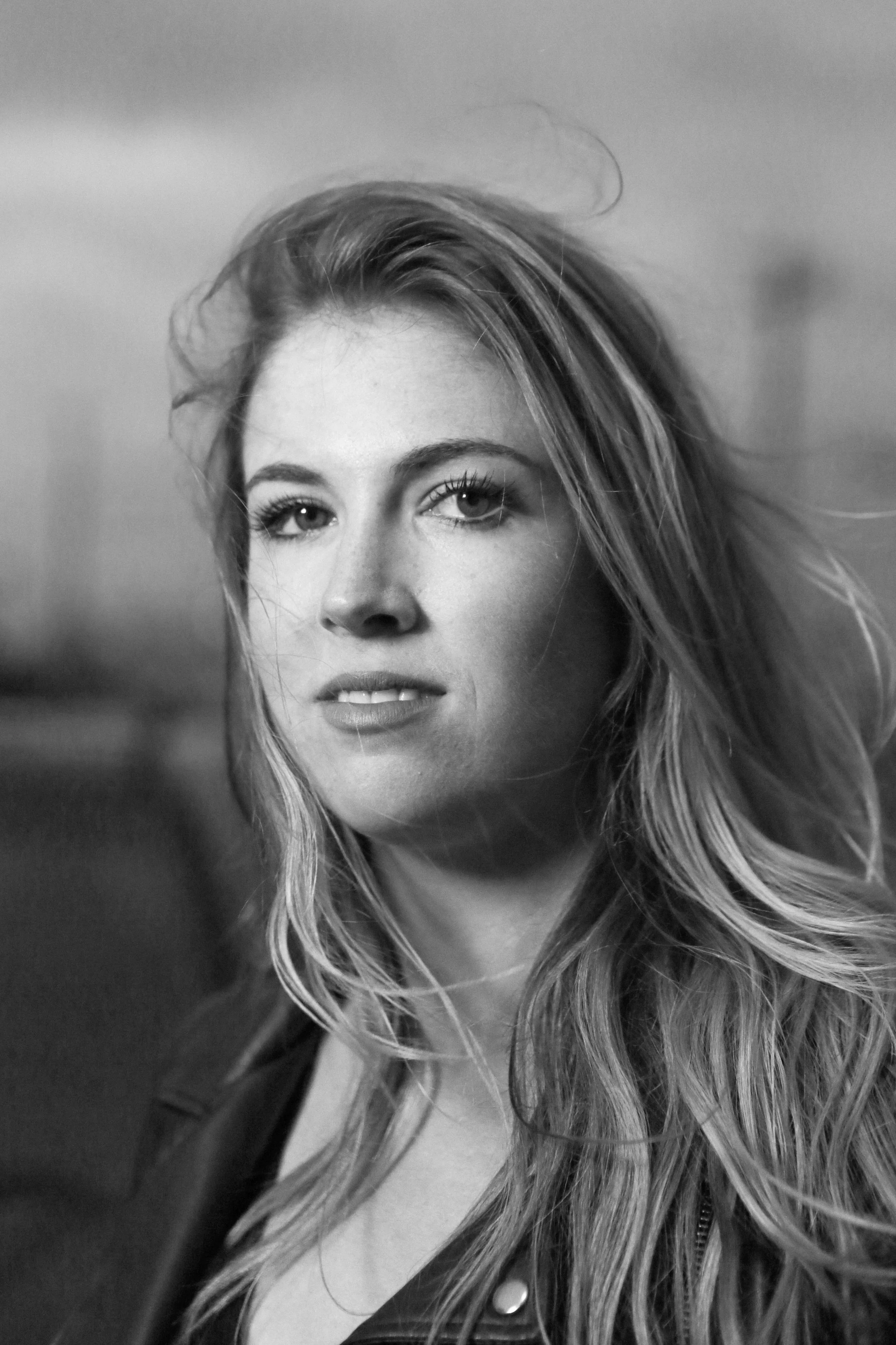 Close-up black and white portrait of a woman with long, wavy hair, looking at the camera with a slight smile.