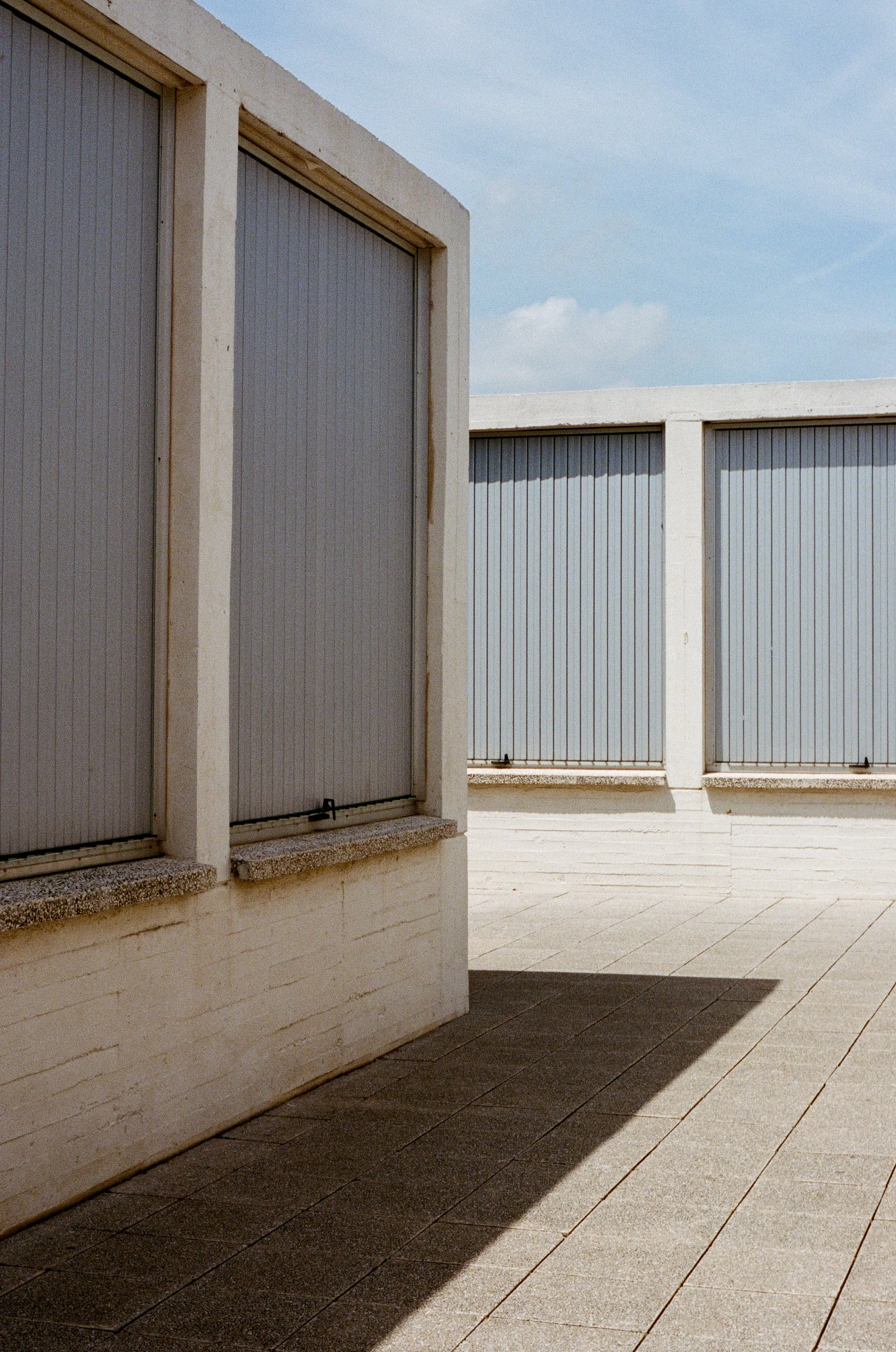 Photo of a white concrete building with three gray roll-down shutters on a sunny day.
