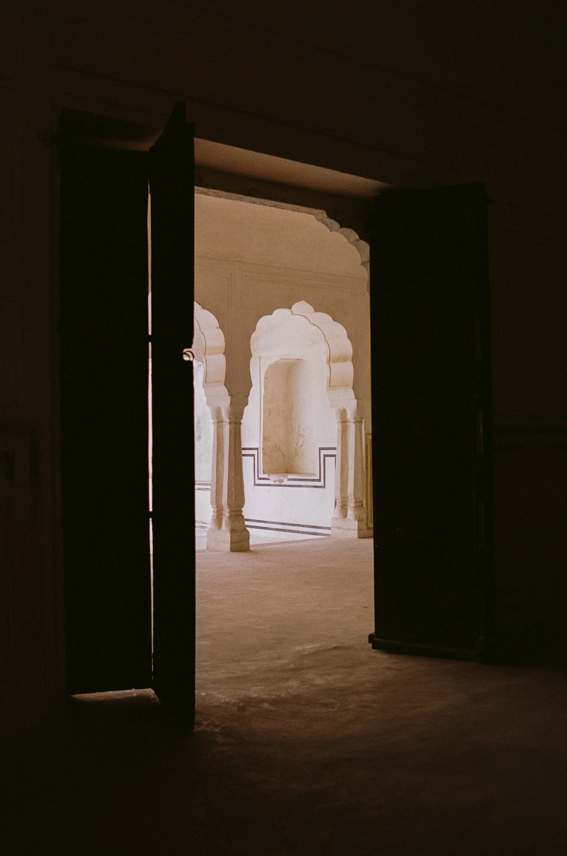 View through an open doorway to a courtyard with white architecture, arches, and columns.