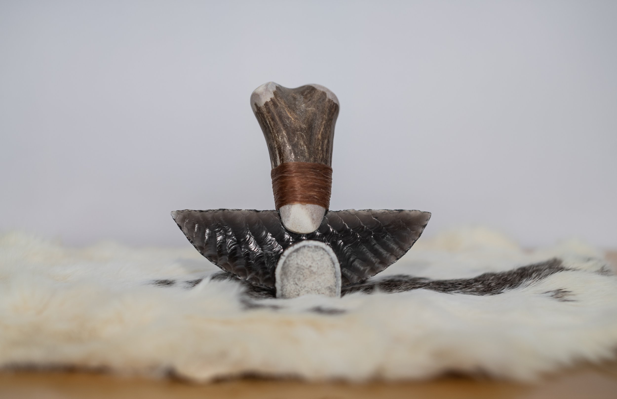 Iconic Alaskan ulu reborn in volcanic obsidian. The sweeping crescent blade is sinew-bound to a naturally curved elk antler handle, complete with a hand-crafted display stand. Timeless northern design meets breathtaking beauty: an heirloom for camp, 