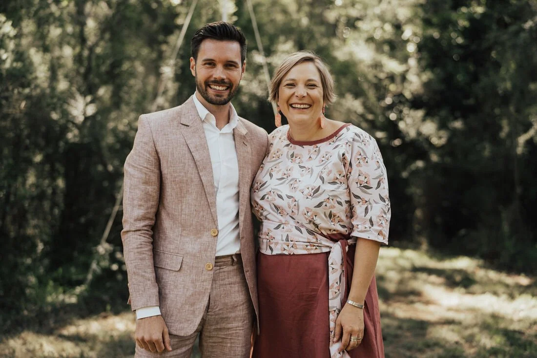 Dee Wild Celebrant and a man are both smiling at the camera. The man is wearing a dusty pink suit and Dee Wild Celebrant is wearing a dusty pink dress.