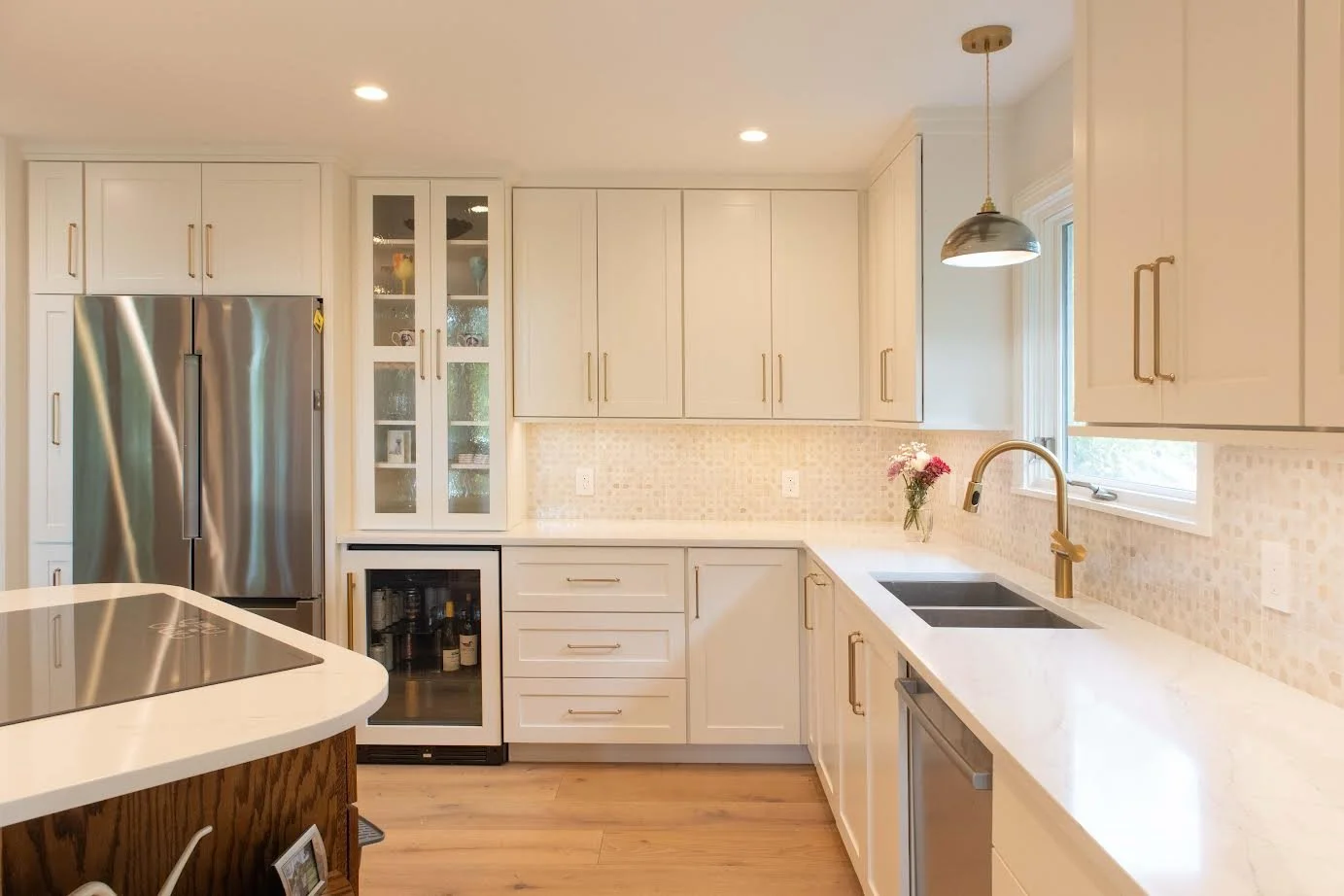 Modern kitchen with white cabinets, stainless steel refrigerator, black sink, white countertops, and a pendant light