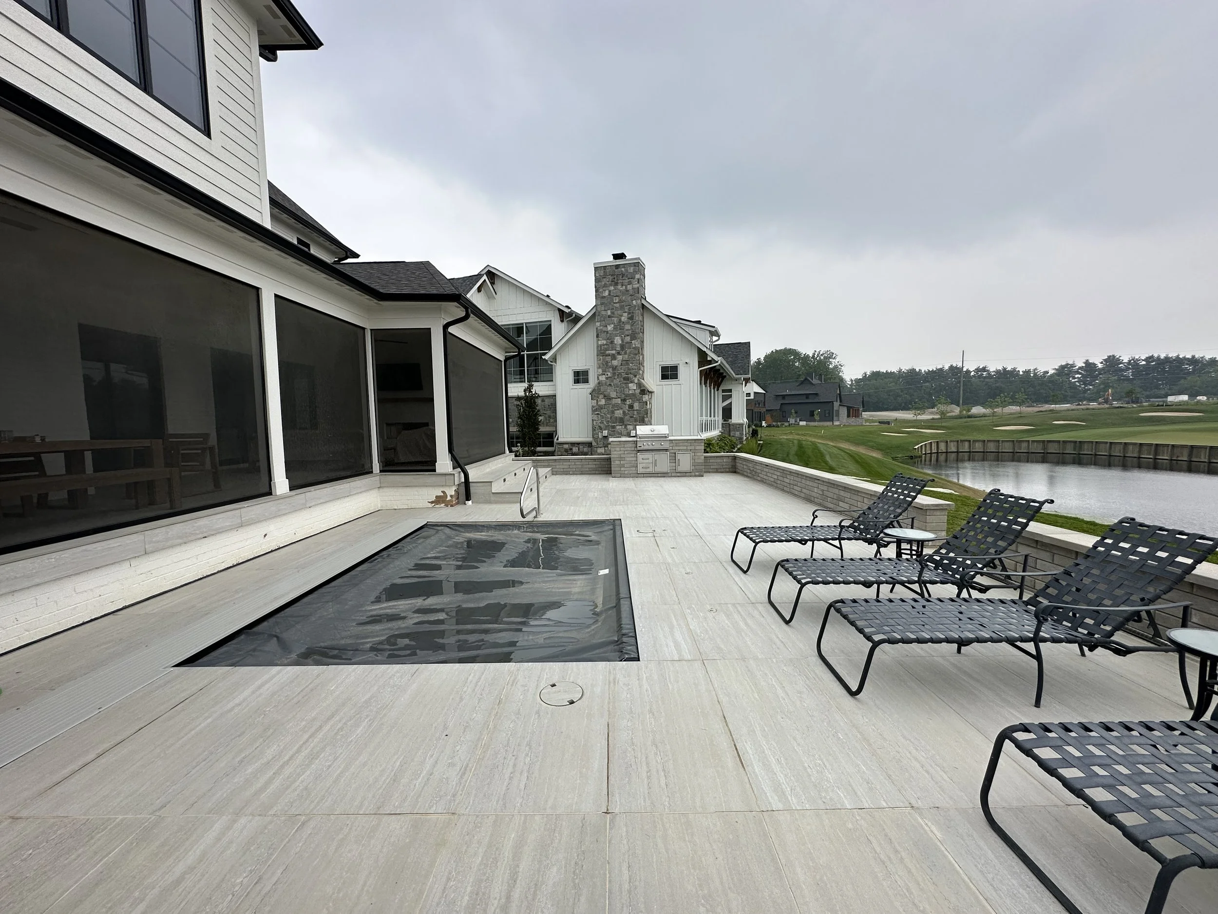Outdoor patio with lounge chairs facing a pond, neighboring houses, and a golf course on a cloudy day.