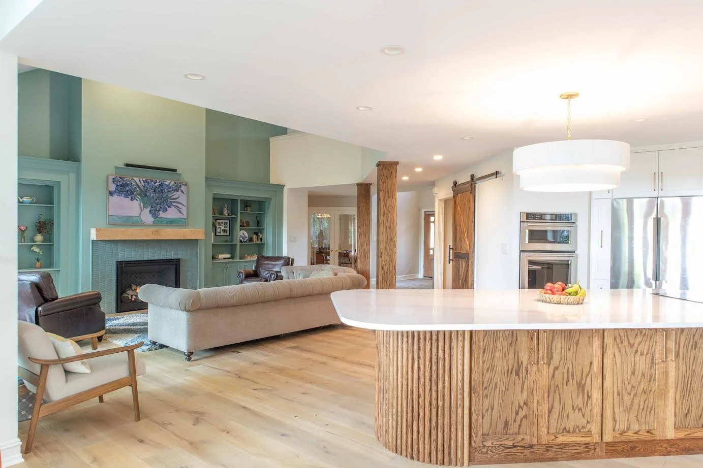 Open-concept living room with built-in shelves, a fireplace, and a kitchen island with a fruit bowl.