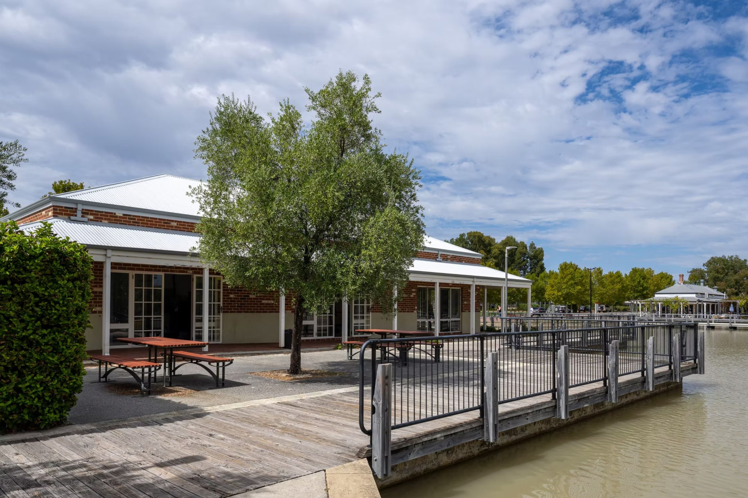 ID: An outside view of The Grapevine. A tree, picnic tables and railing are in the midground. 