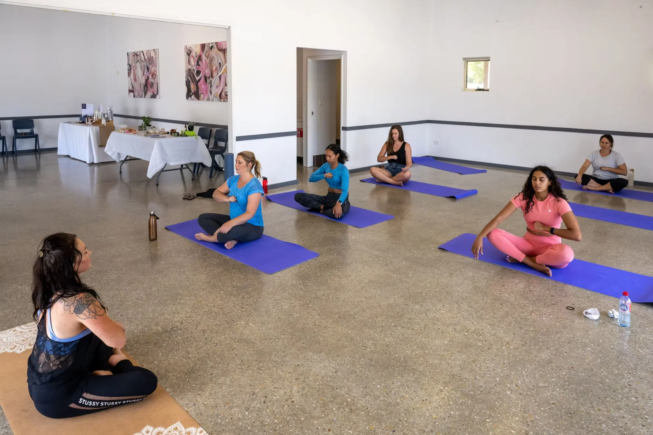 ID: A yoga class. The instructor and participants sit on mats.