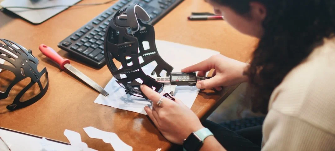 A person measuring a black, skeletal helmet with a digital caliper on a cluttered desk.