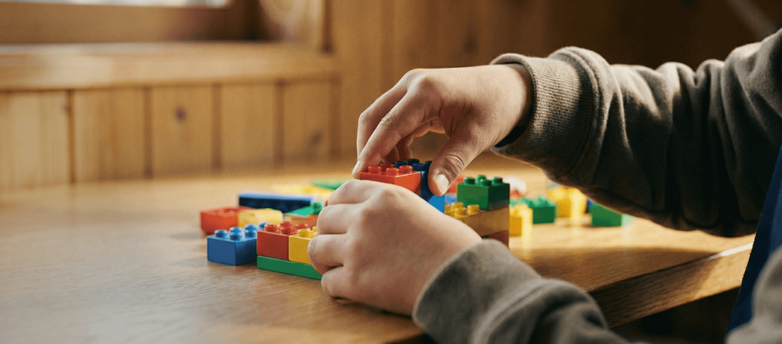 Person's hands assembling colorful Lego bricks on a wooden table.