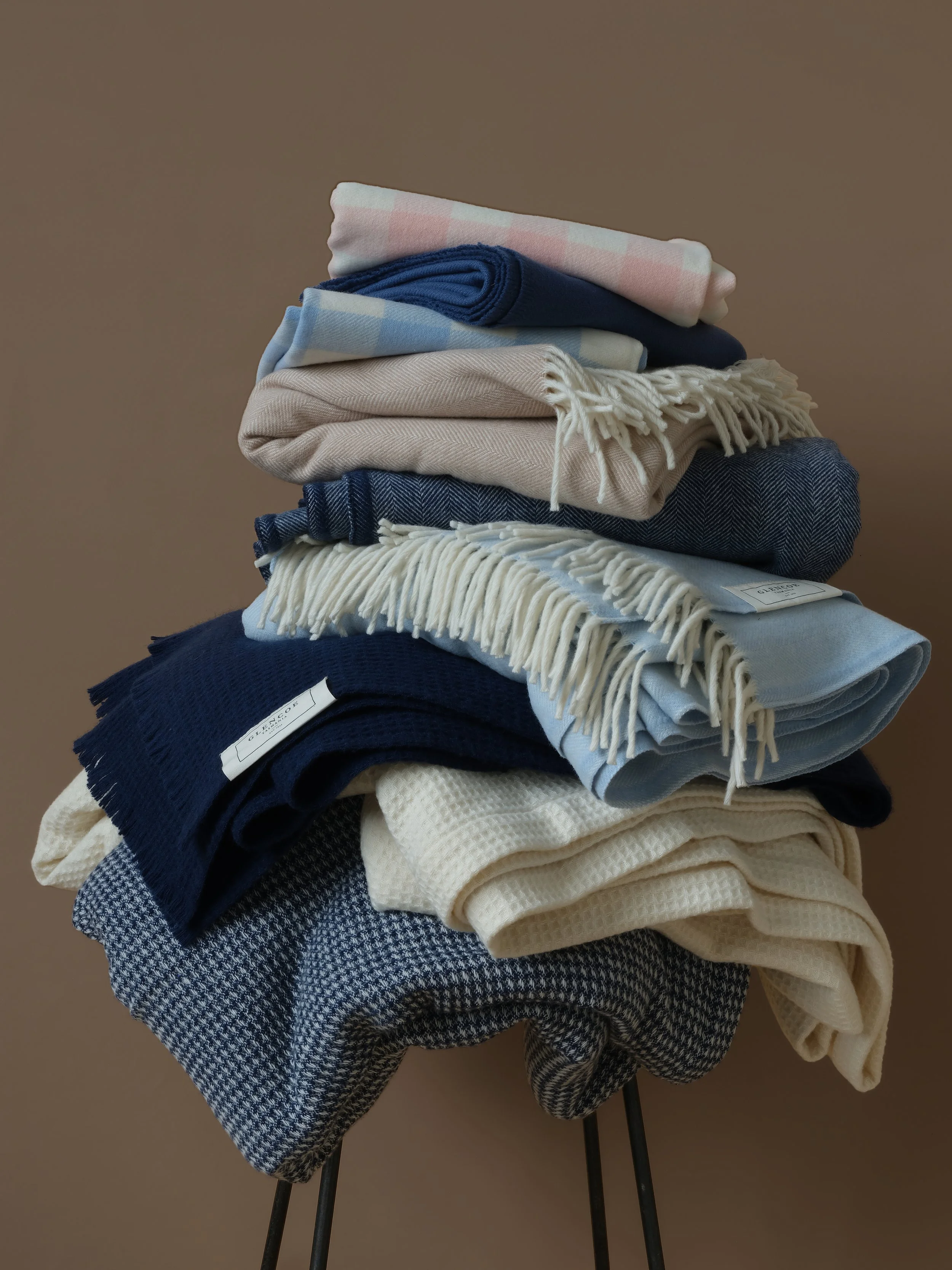 A stack of folded clothes, including scarves and fabrics, placed on a stand against a plain background.