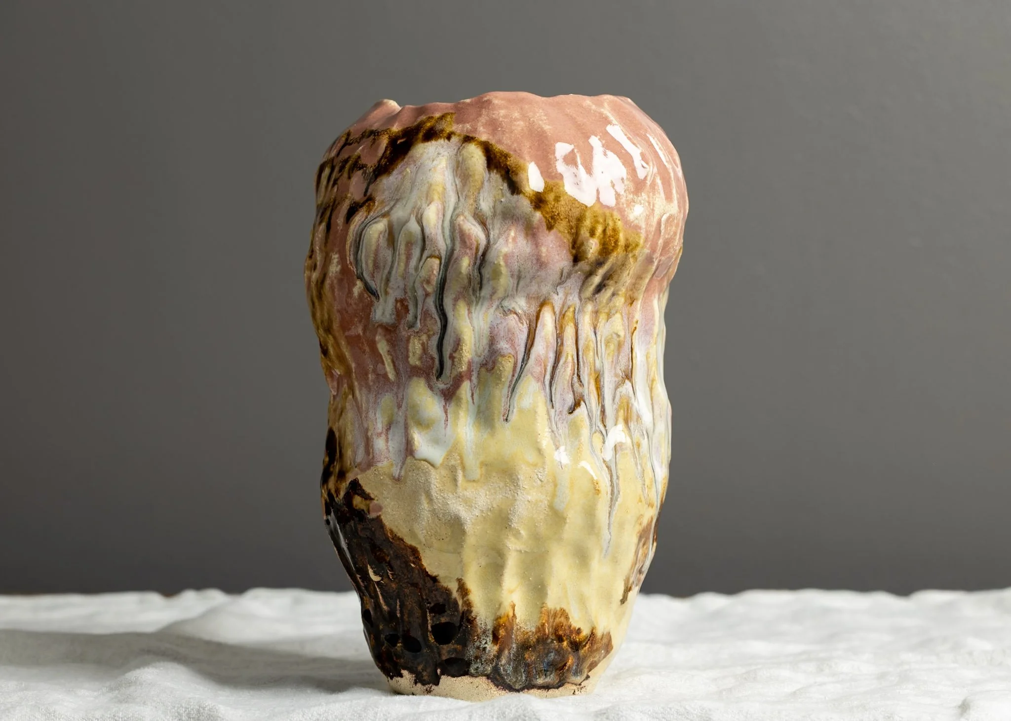 A piece of wood with a smooth, polished surface showcasing swirling patterns of beige, white, brown, and pinkish tones, placed on a white textured surface against a plain grey background.