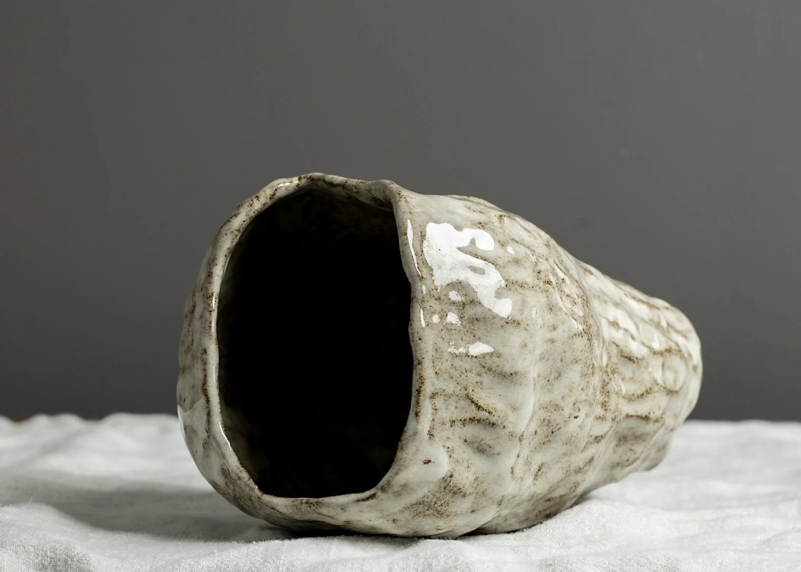 A seashell-shaped ceramic mug with an open top, lying on its side on a white surface against a plain gray background.