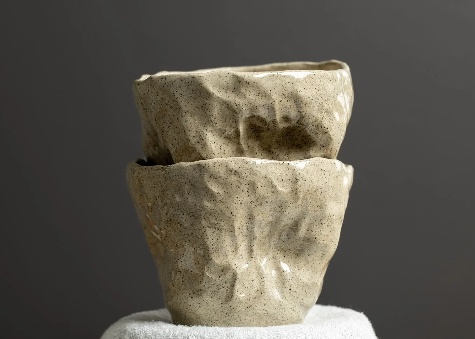 Close-up of two handmade ceramic bowls stacked together, with a textured, speckled beige surface, against a solid gray background.